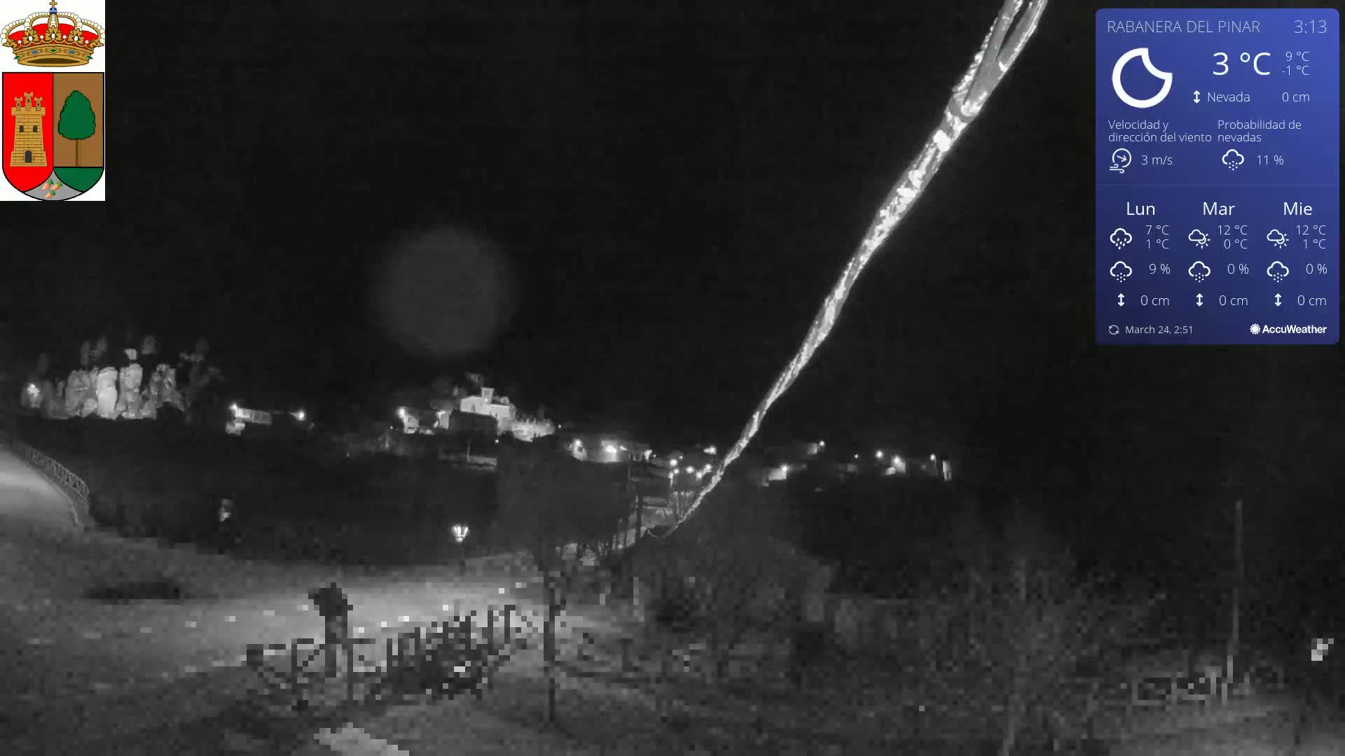 A nighttime, snowy scene shows a small town illuminated by scattered lights, with a bright streak in the sky.
