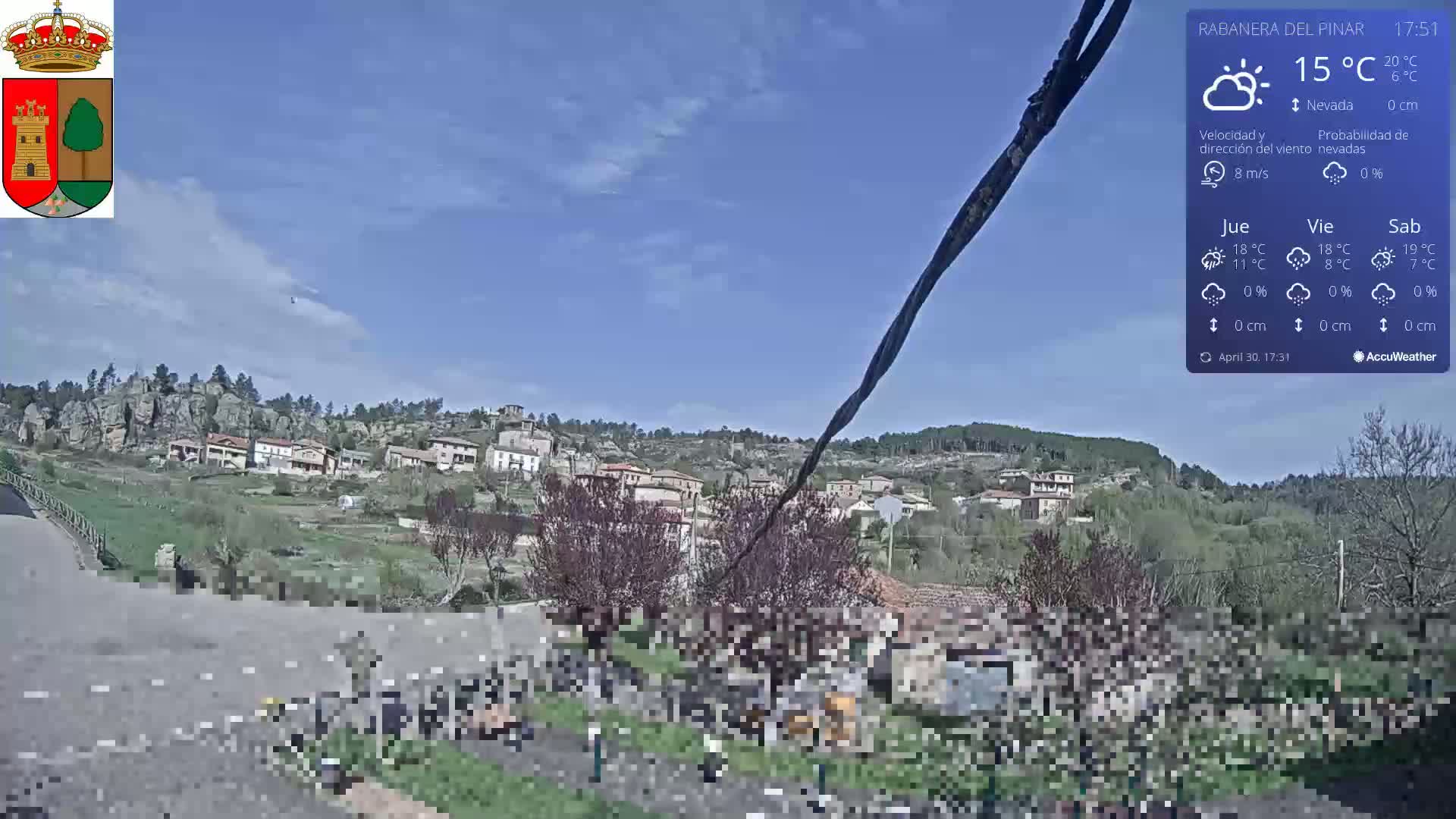A small village nestled in a hilly landscape under a mostly clear, sunny sky.