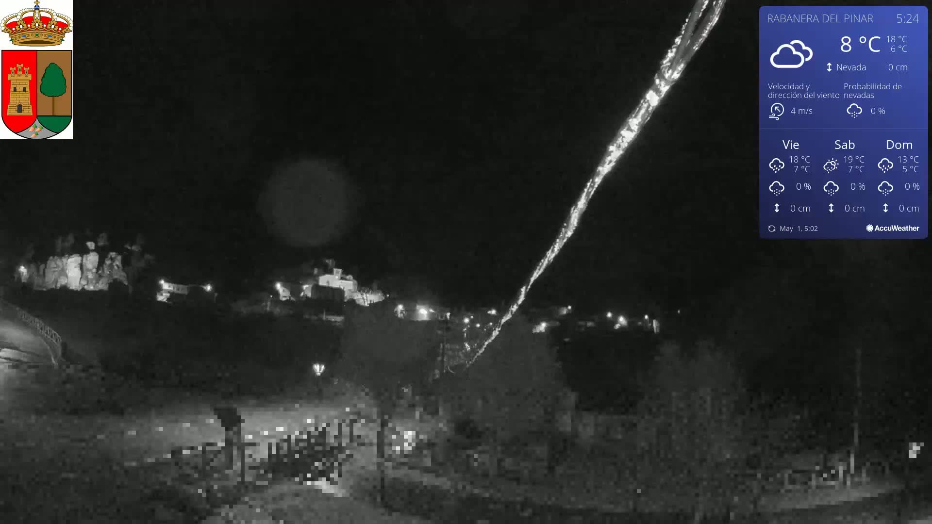 A nighttime, low-light view of a town with a bright streak of light in the sky, under mostly clear skies.