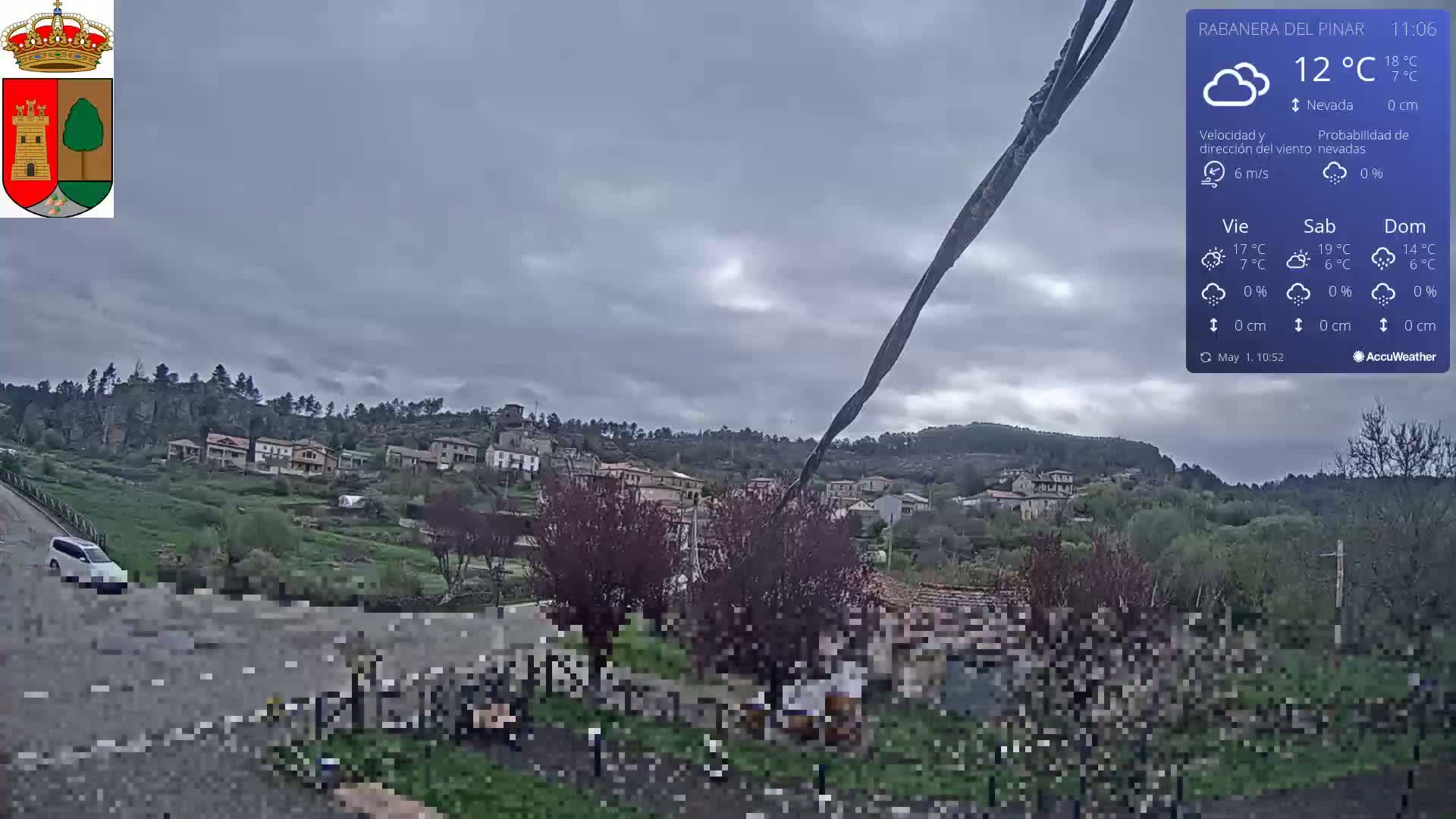 A cloudy, overcast day reveals a small village nestled on a hillside, with a few people gathered near some buildings in the foreground.