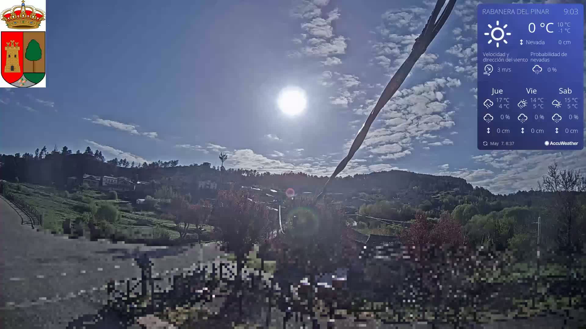 A sunny day with a few clouds over a small village nestled among green hills.