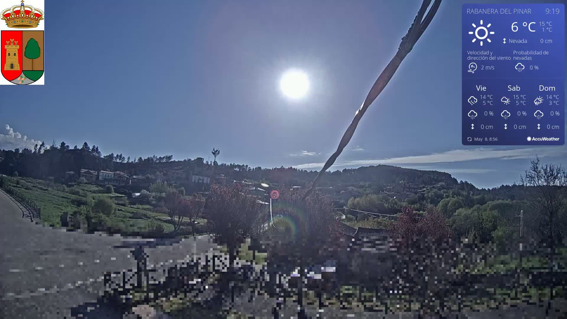 A sunny, clear day overlooks a small village nestled in a green, hilly landscape.
