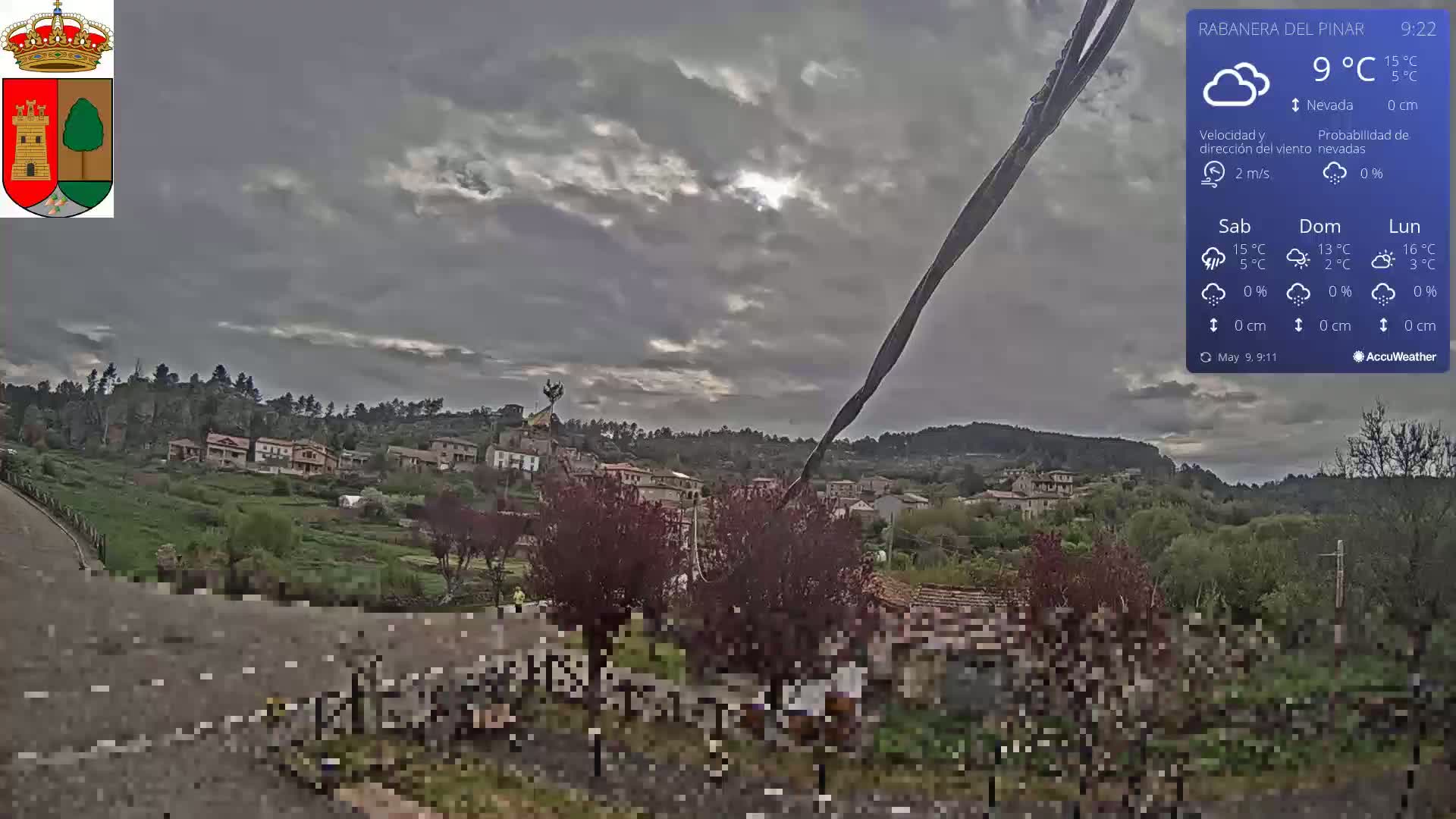 A partly cloudy, cool day reveals a small village nestled in a valley surrounded by hills and trees.