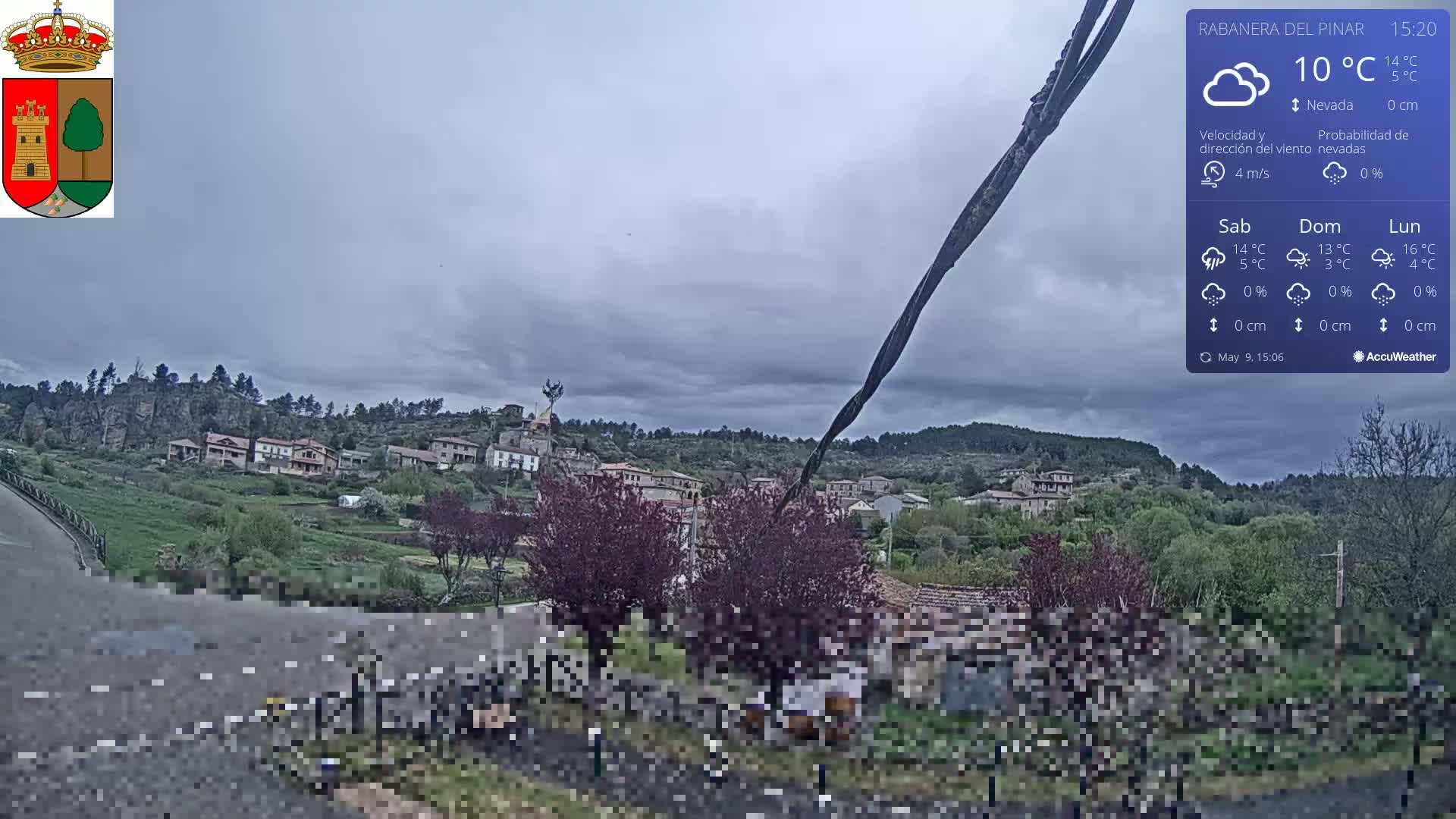 A small village nestled on a hillside under an overcast sky is viewed from a slightly elevated vantage point.
