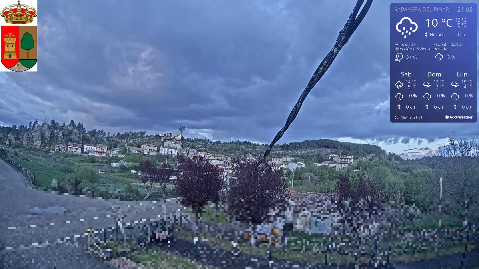 A small town nestled in a hilly landscape under a mostly cloudy, dark sky.
