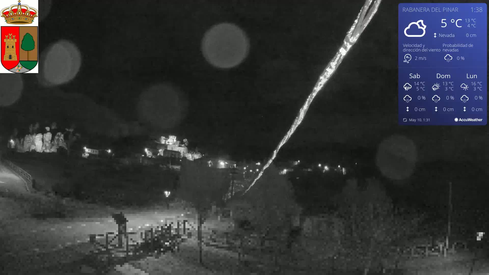 A nighttime, snowy scene shows a small town nestled in a hill, with a bright streak of light cutting across the dark sky.