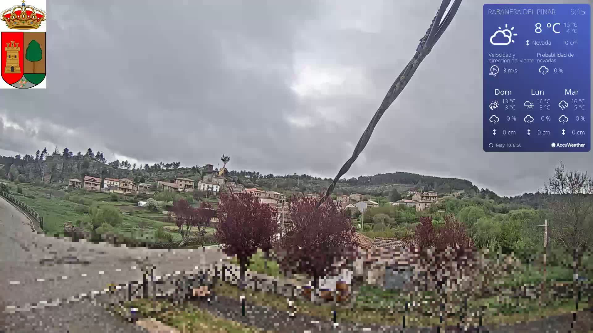 A small village nestled in a green valley under an overcast sky is viewed from a slightly elevated position.