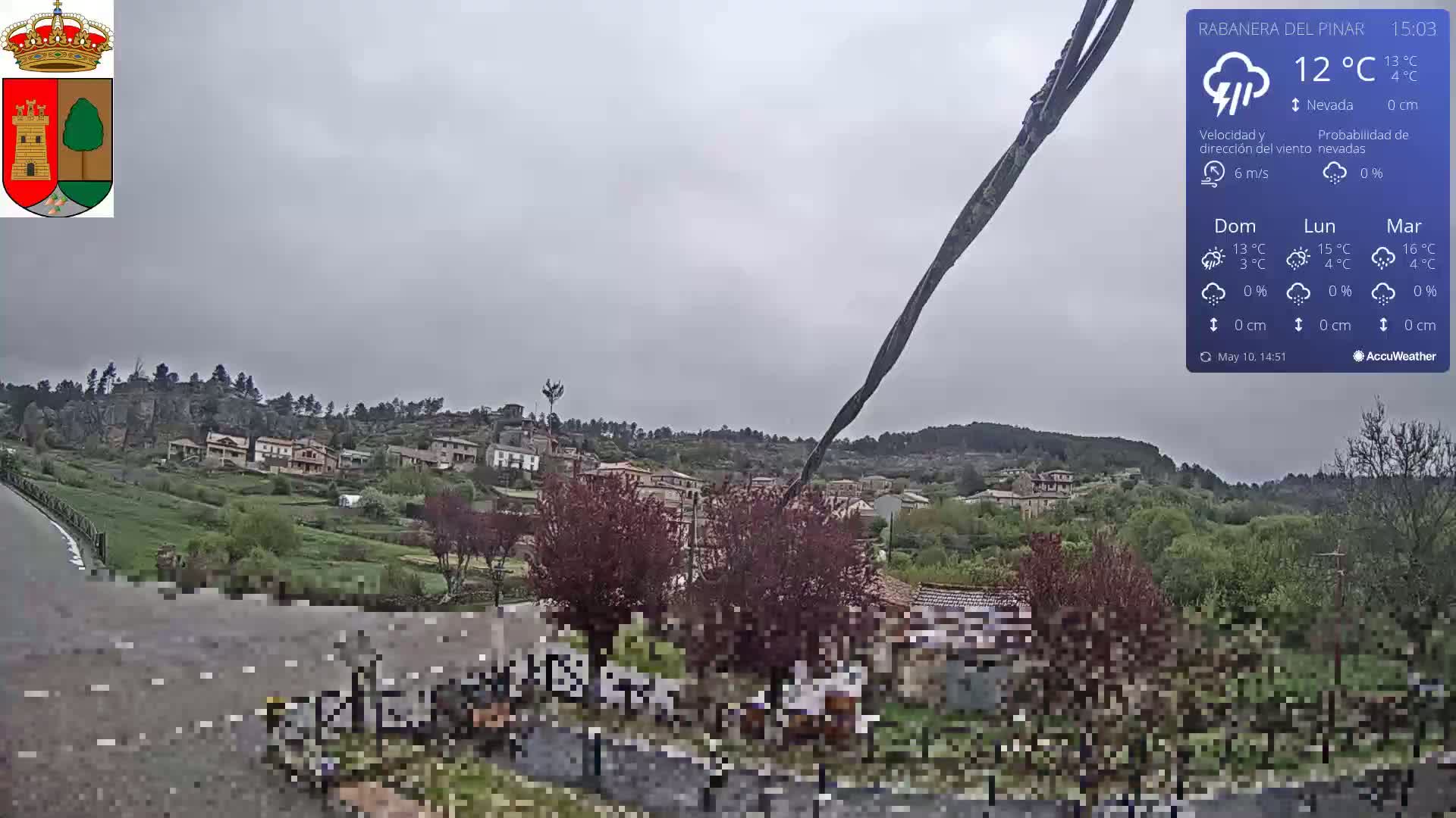 A small village nestled on a hillside is visible under an overcast sky, with a long dark object extending diagonally across the foreground.