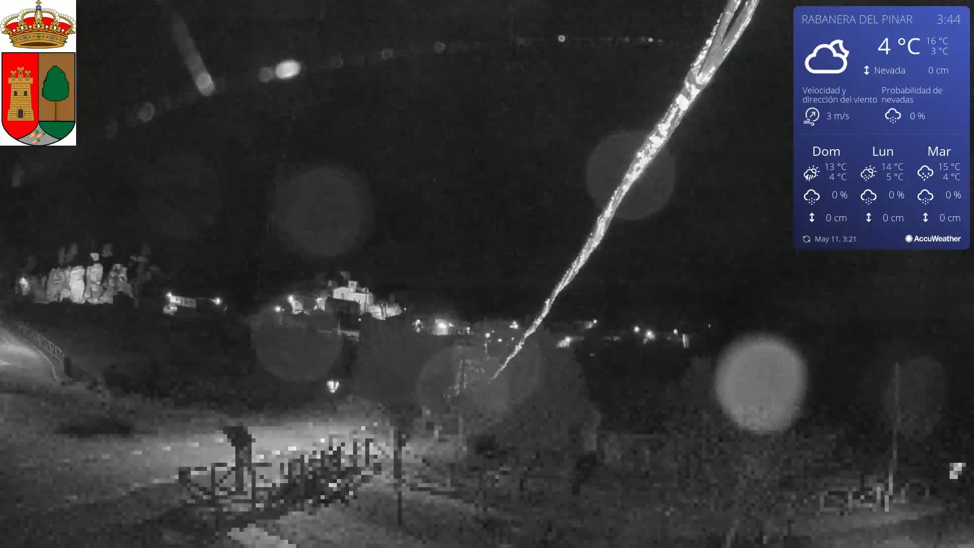 A nighttime, snowy scene shows a long, bright streak in the dark sky above a dimly lit town.