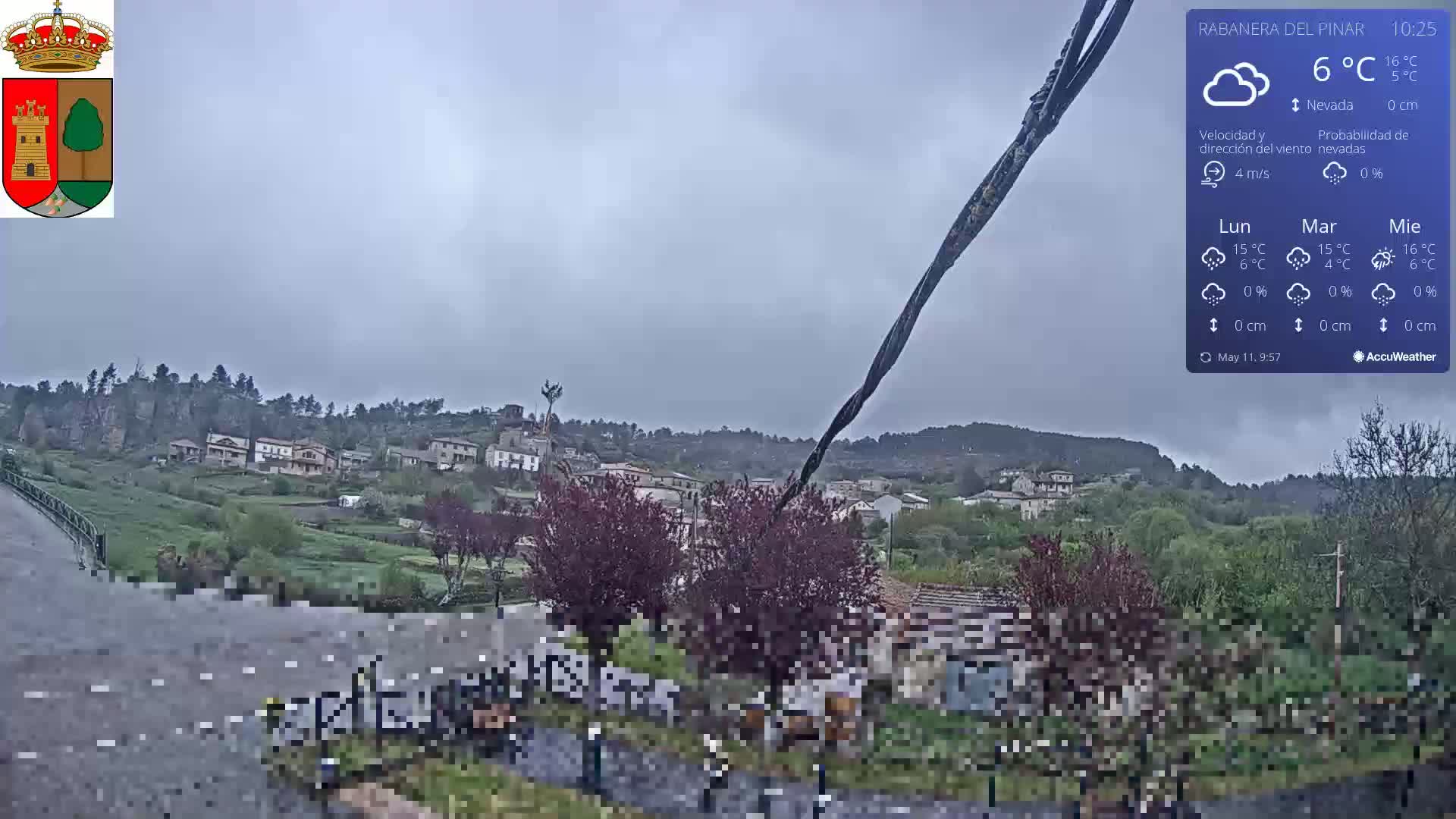 A small village nestled on a hillside is visible under an overcast sky, with light rain falling.