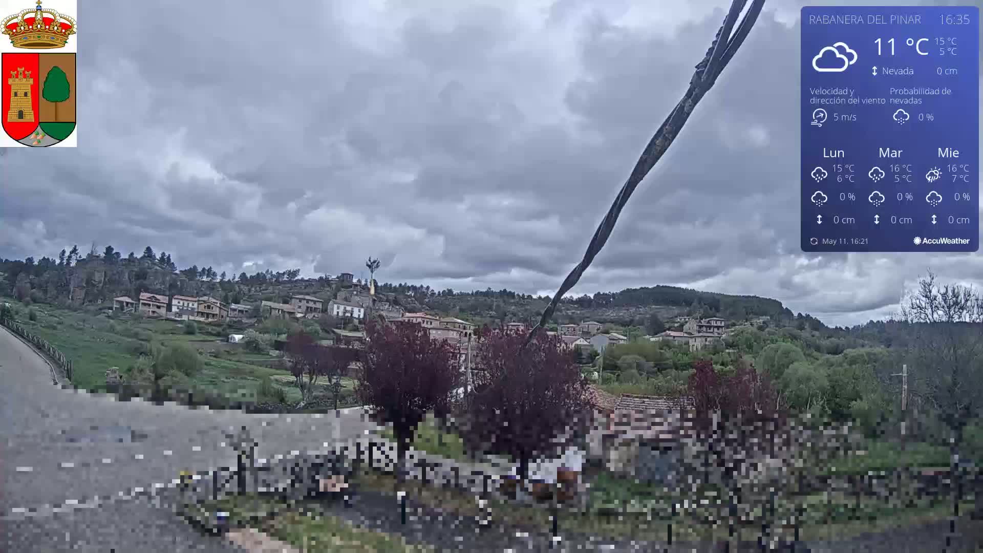 A small village nestled on a hillside under a cloudy sky is viewed from a slightly elevated vantage point.