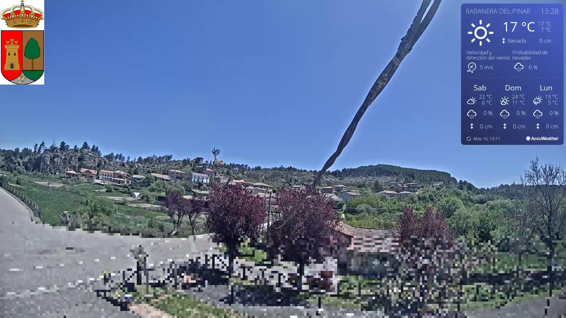 A sunny, clear day overlooks a small village nestled in a hilly, green landscape.