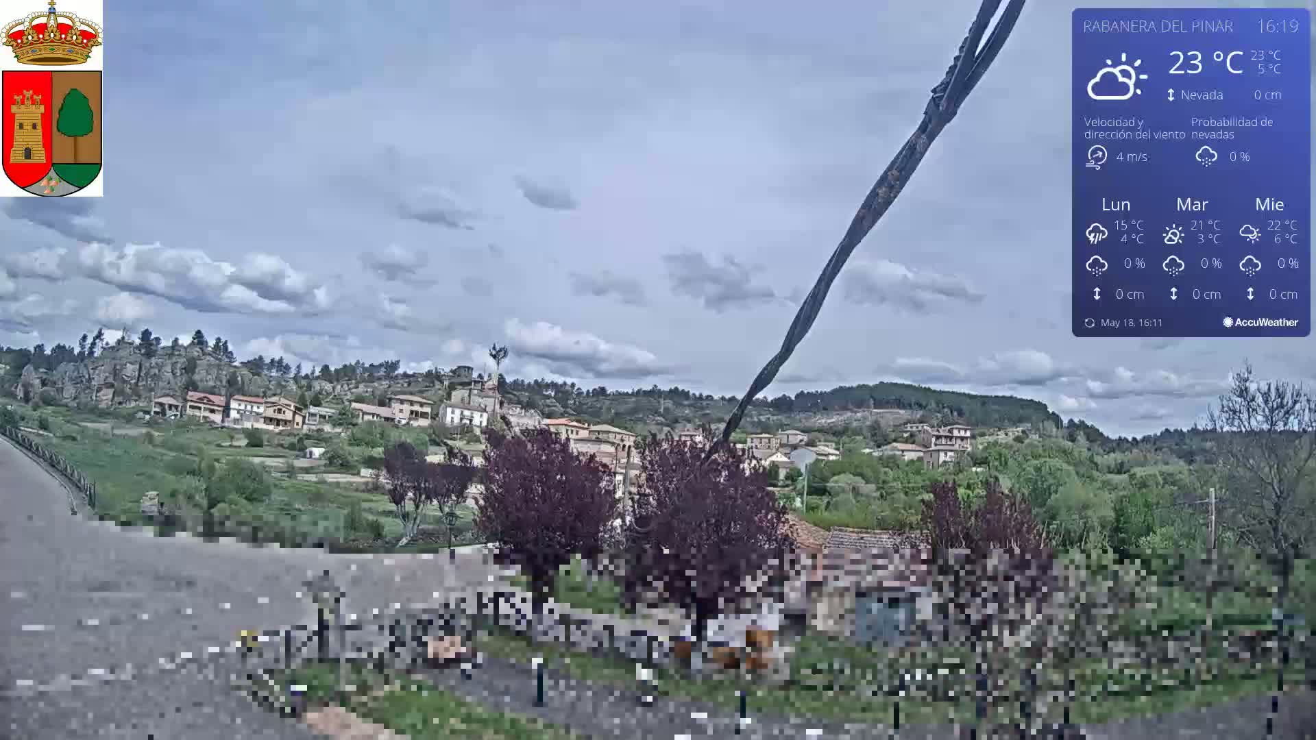A partly cloudy day reveals a small village nestled in a green valley, surrounded by rocky hills.