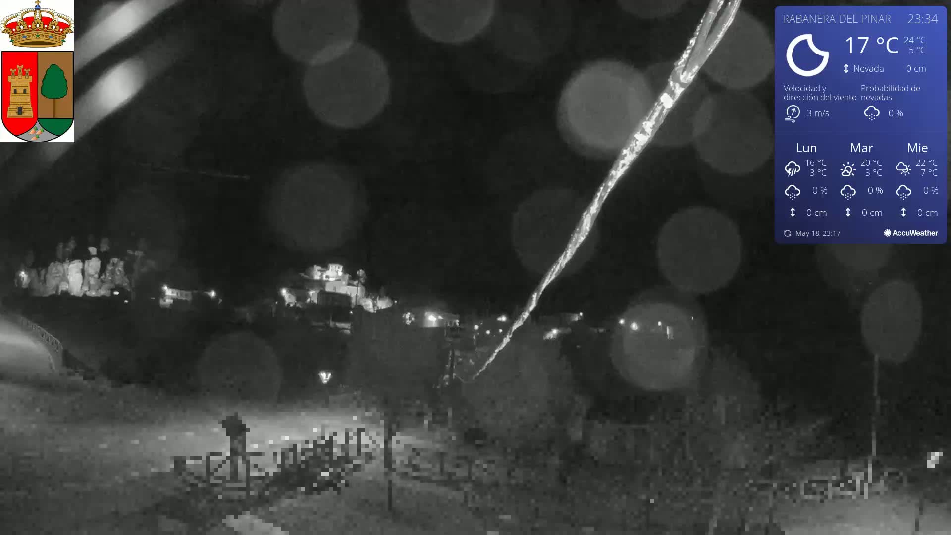 A nighttime, snowy scene shows a small town illuminated with faint lights under a dark sky, with a long streak of something bright, possibly ice, falling from above.