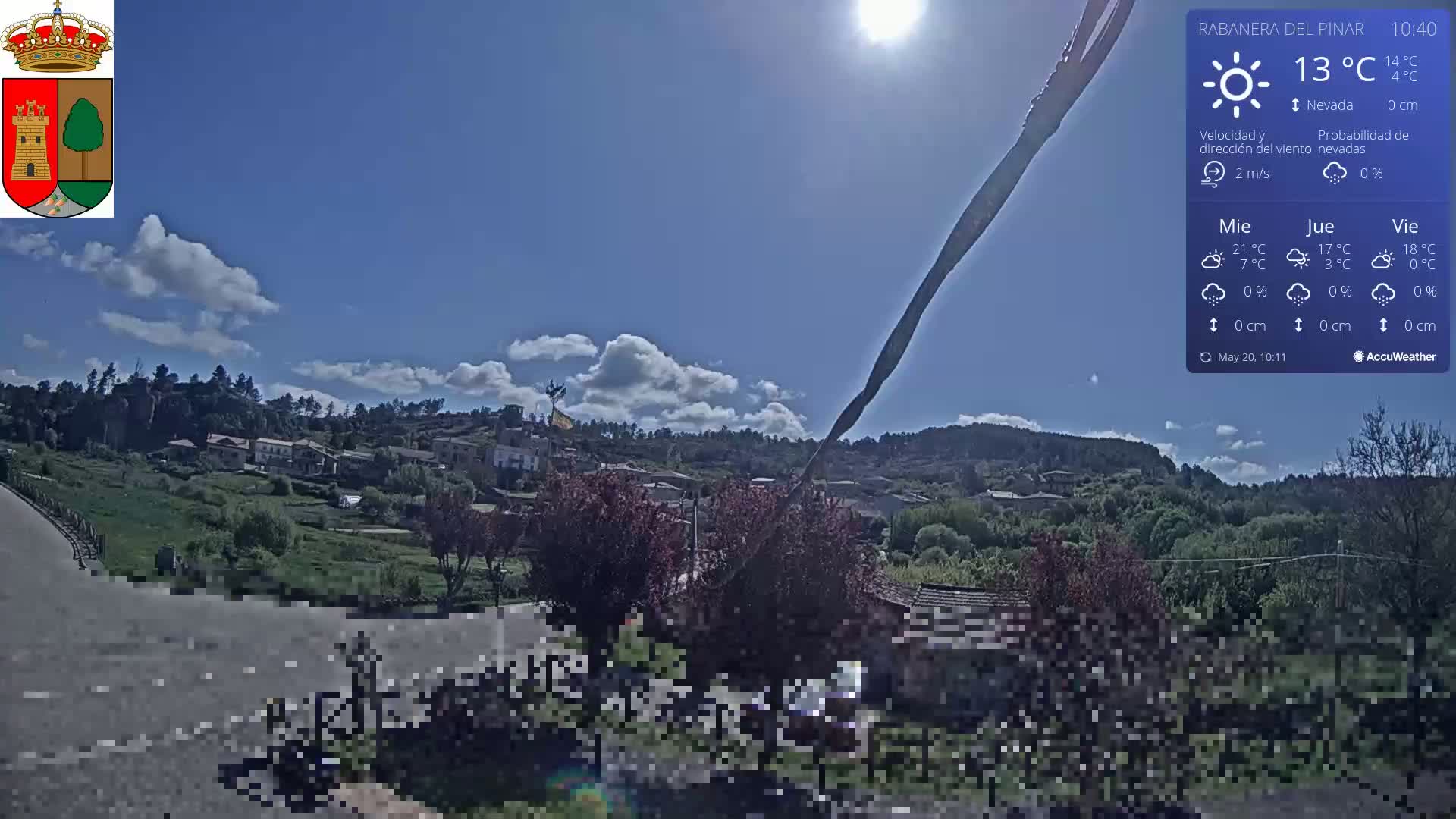 A sunny day with some clouds reveals a small village nestled in a green valley, with a road in the foreground.