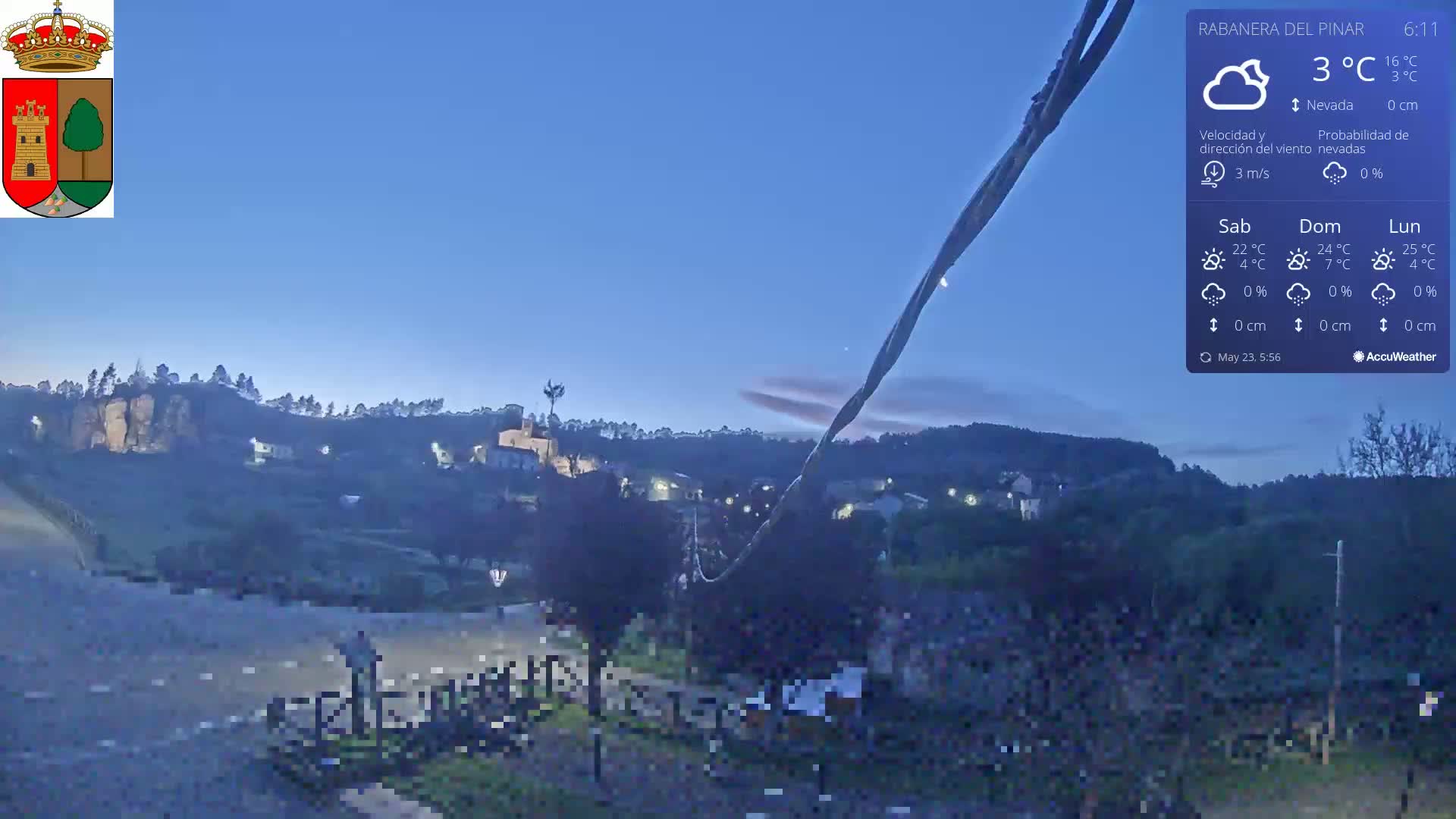 A nighttime view of a small village nestled in a hilly landscape under a clear, twilight sky with a temperature of 3°C.