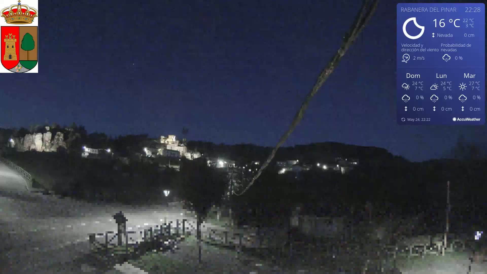 A nighttime view of a small town nestled in a hilly landscape under a clear, dark blue sky.