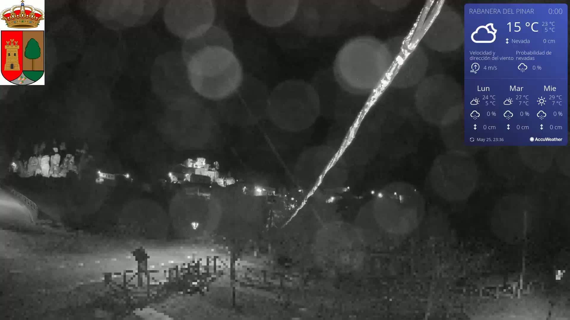 A nighttime, snowy scene shows a small town with faint lights, a dark road, and a streak of falling snow or ice visible in the foreground.