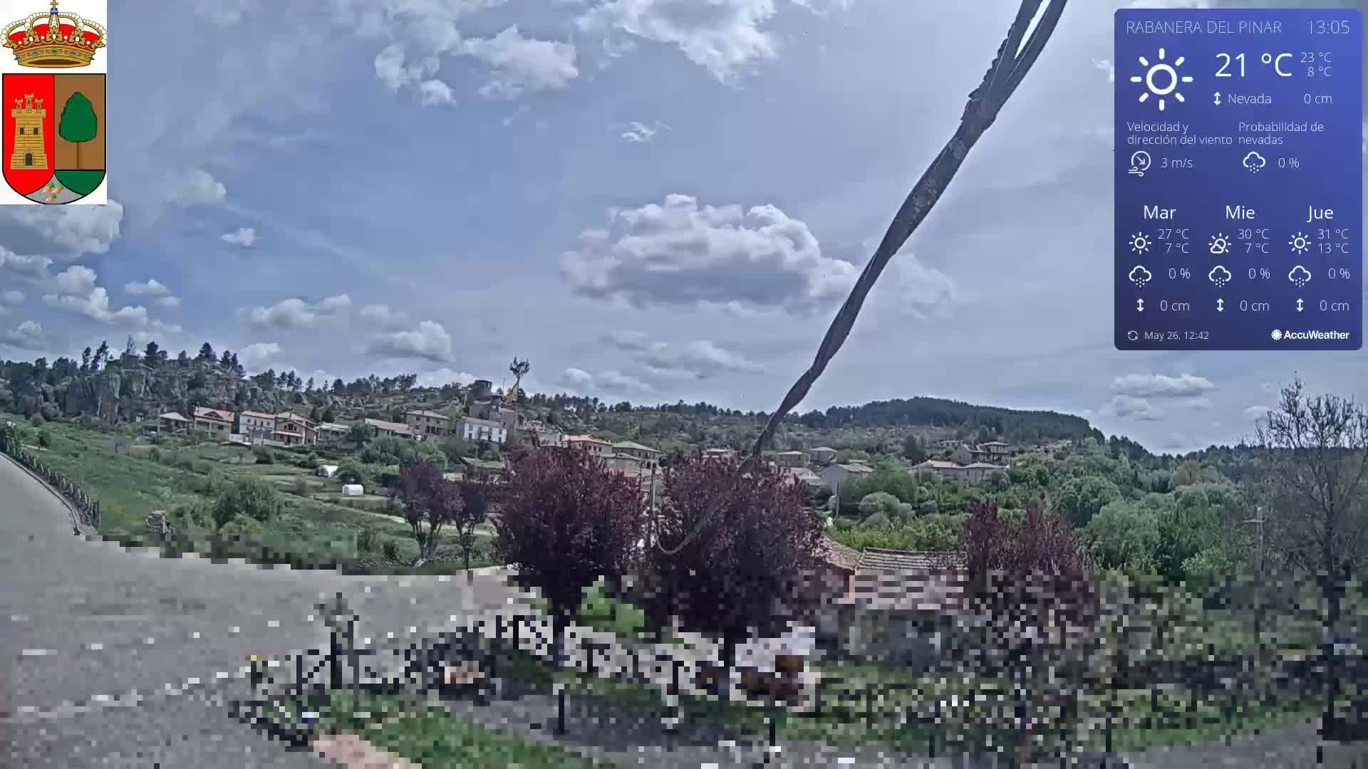 A partly cloudy day reveals a small village nestled in a hilly, green landscape.