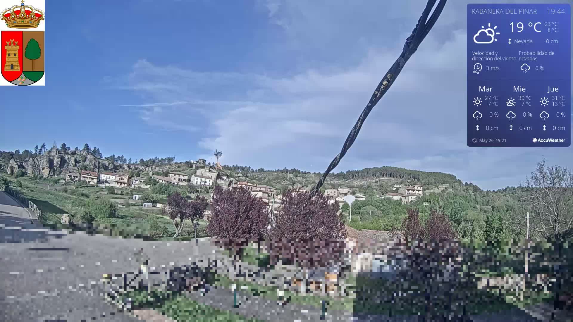 A small village nestled on a hillside under a mostly clear blue sky with a few scattered clouds.