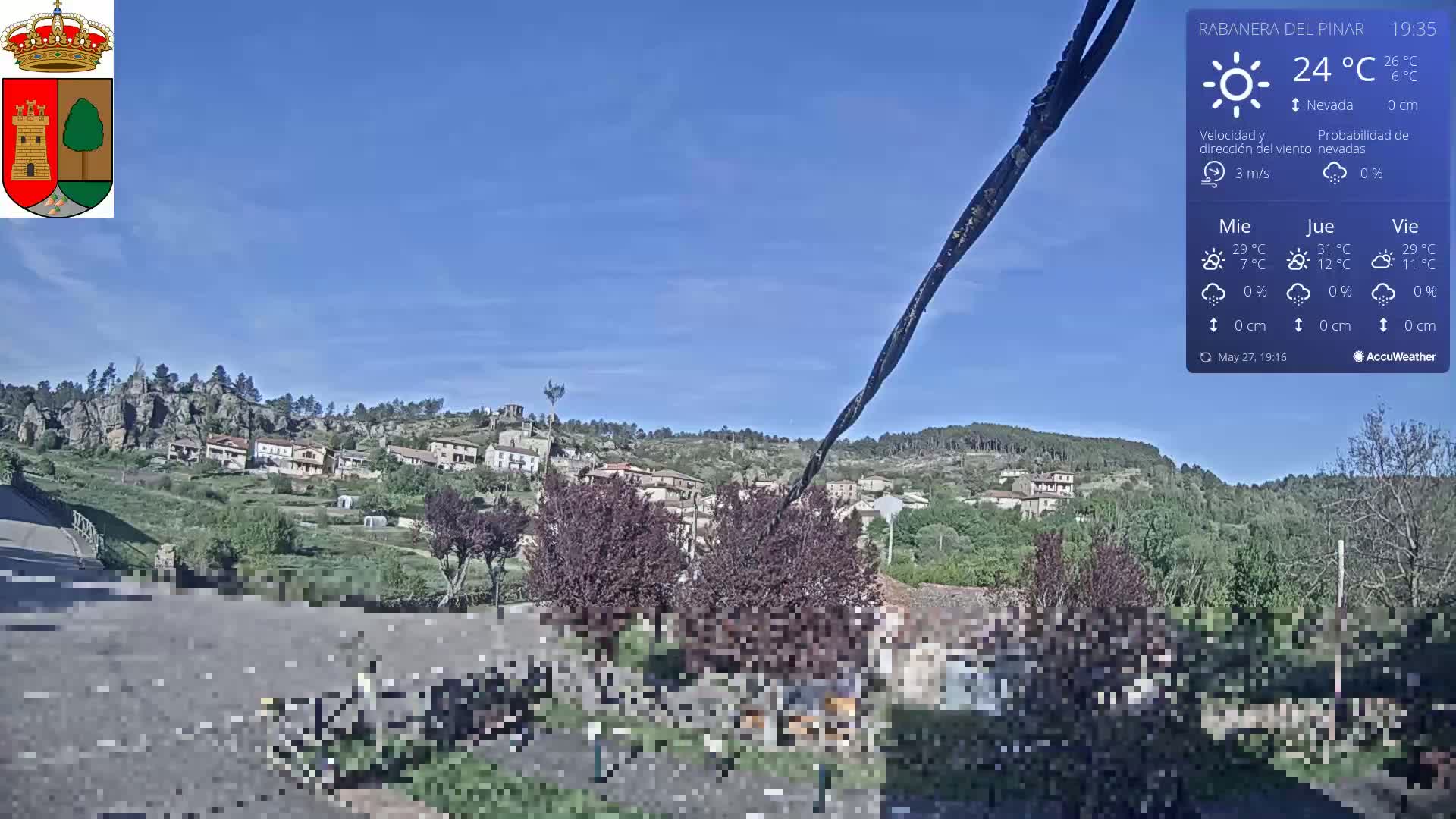 A small village nestled on a hillside under a clear blue sky is visible from a slightly elevated vantage point.