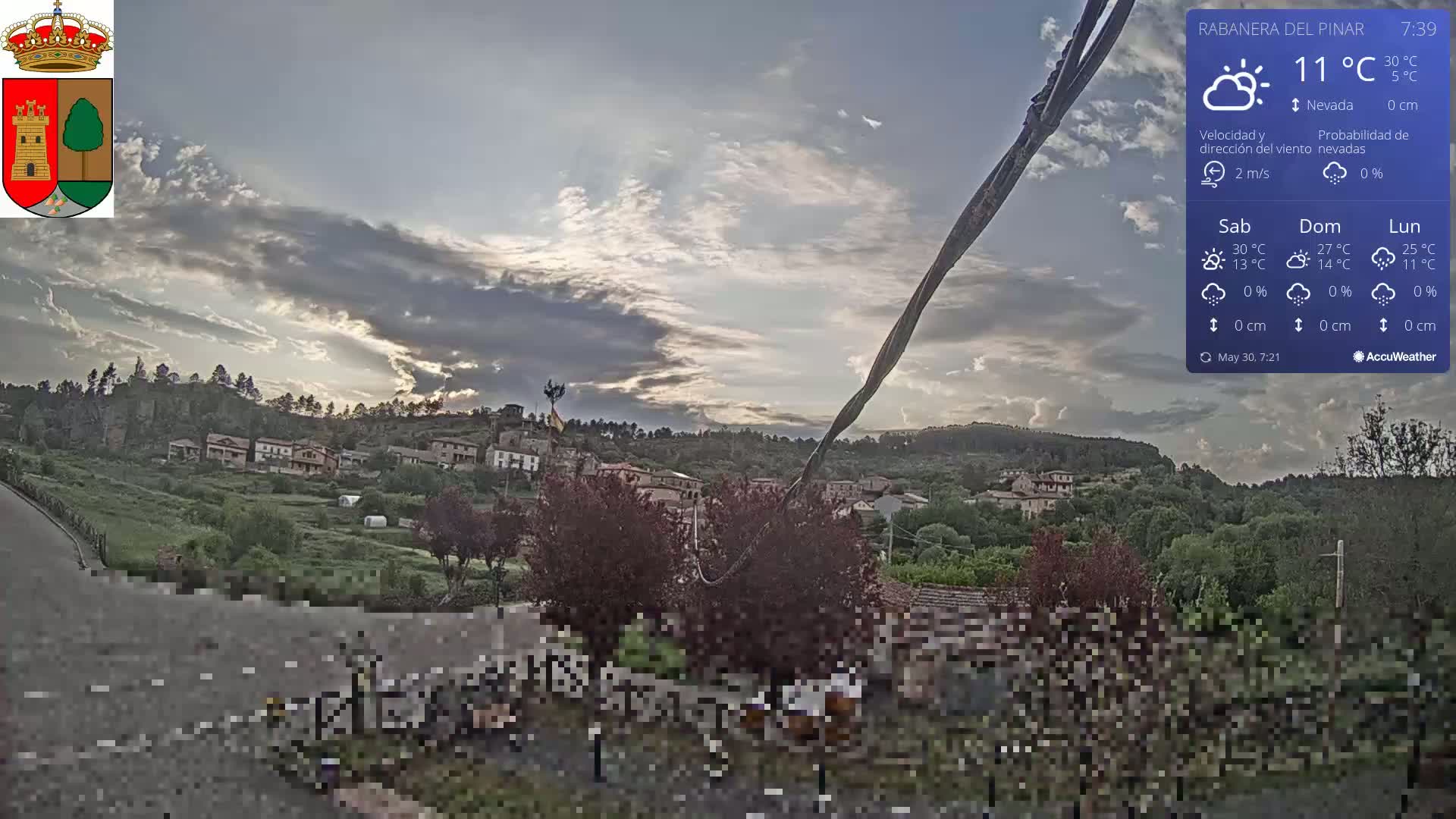 A partly cloudy sky over a small village nestled in a green hillside.