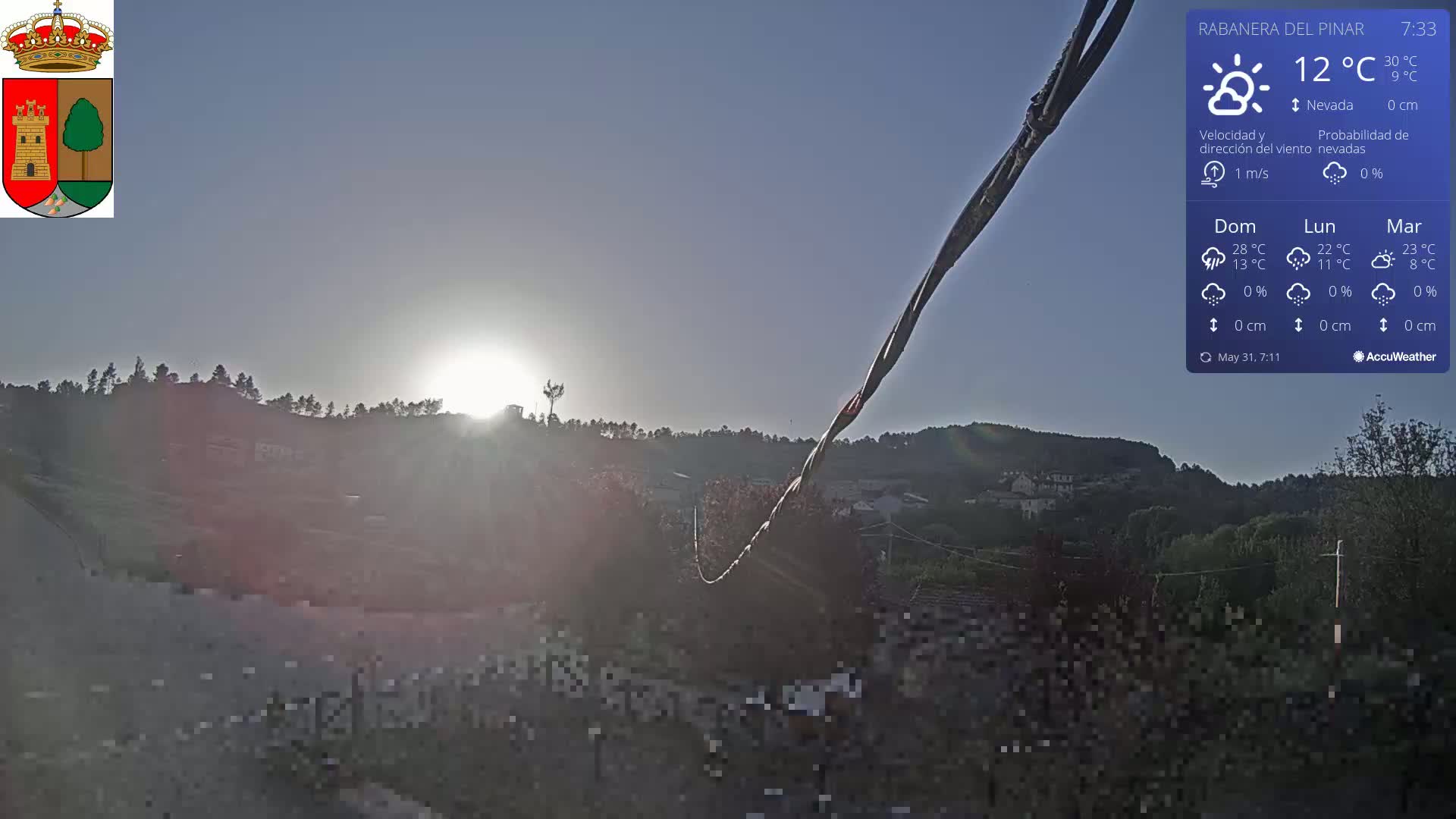 A bright sunrise illuminates a hilly landscape covered in vegetation, under a clear sky.