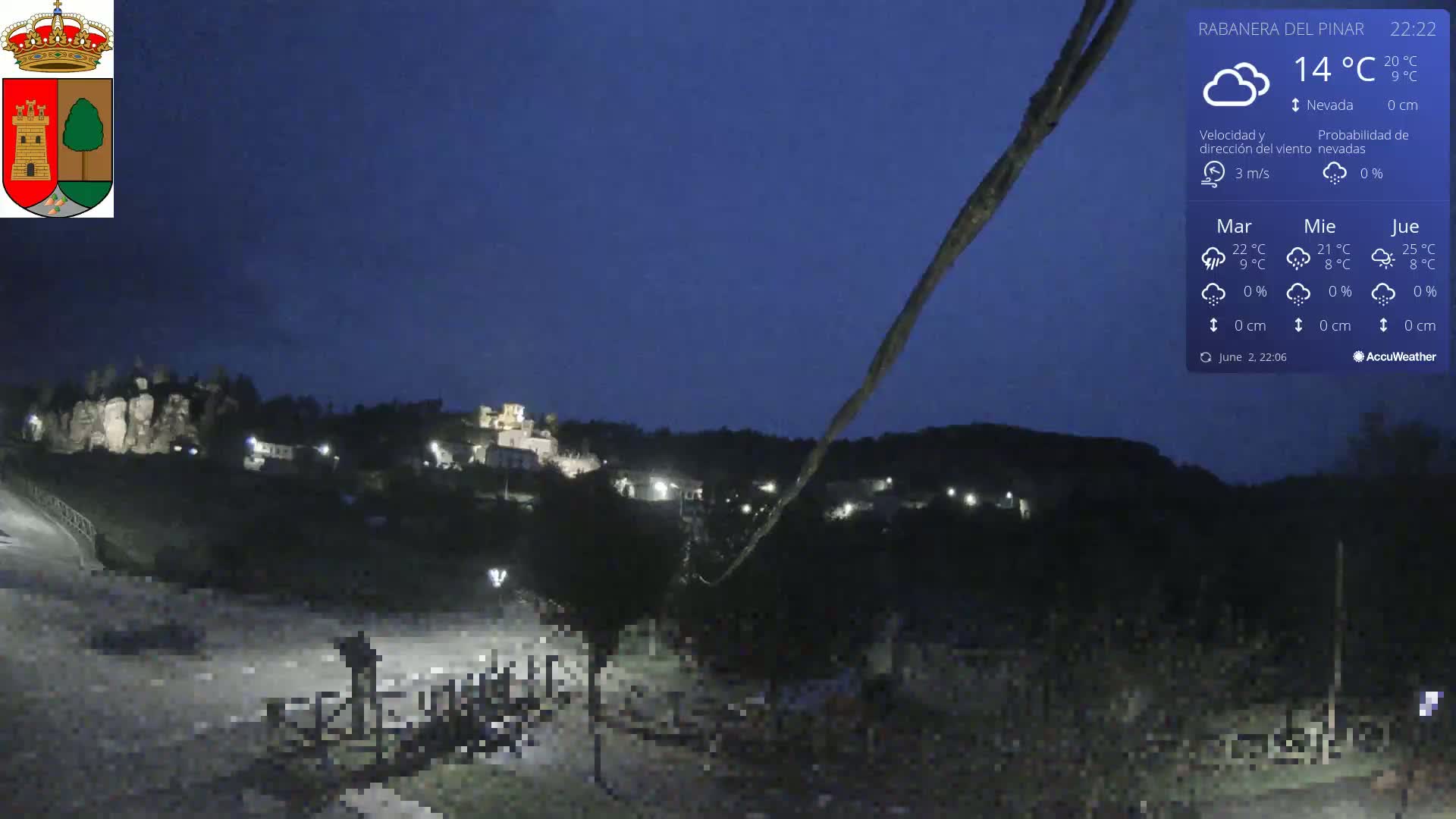 A nighttime view of a small town nestled among hills under a clear, dark blue sky.