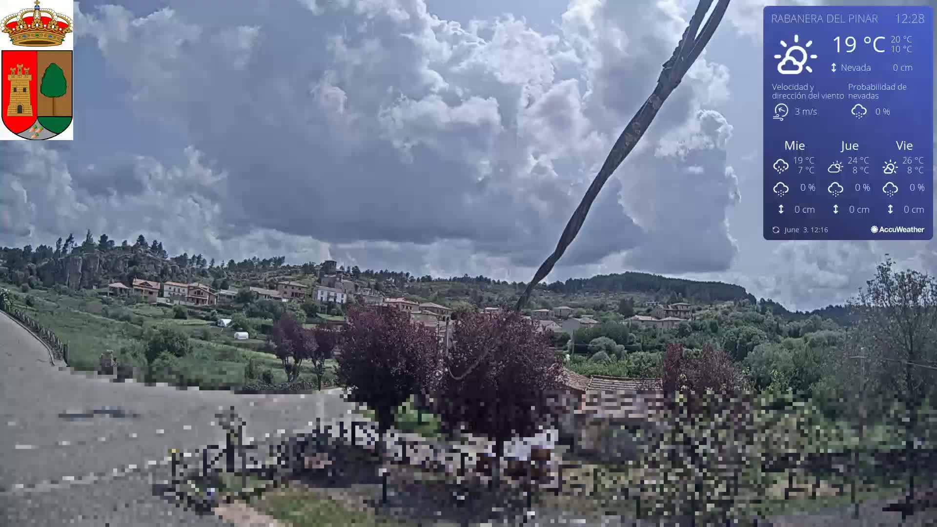 A partly cloudy sky over a small town nestled among green hills and trees.