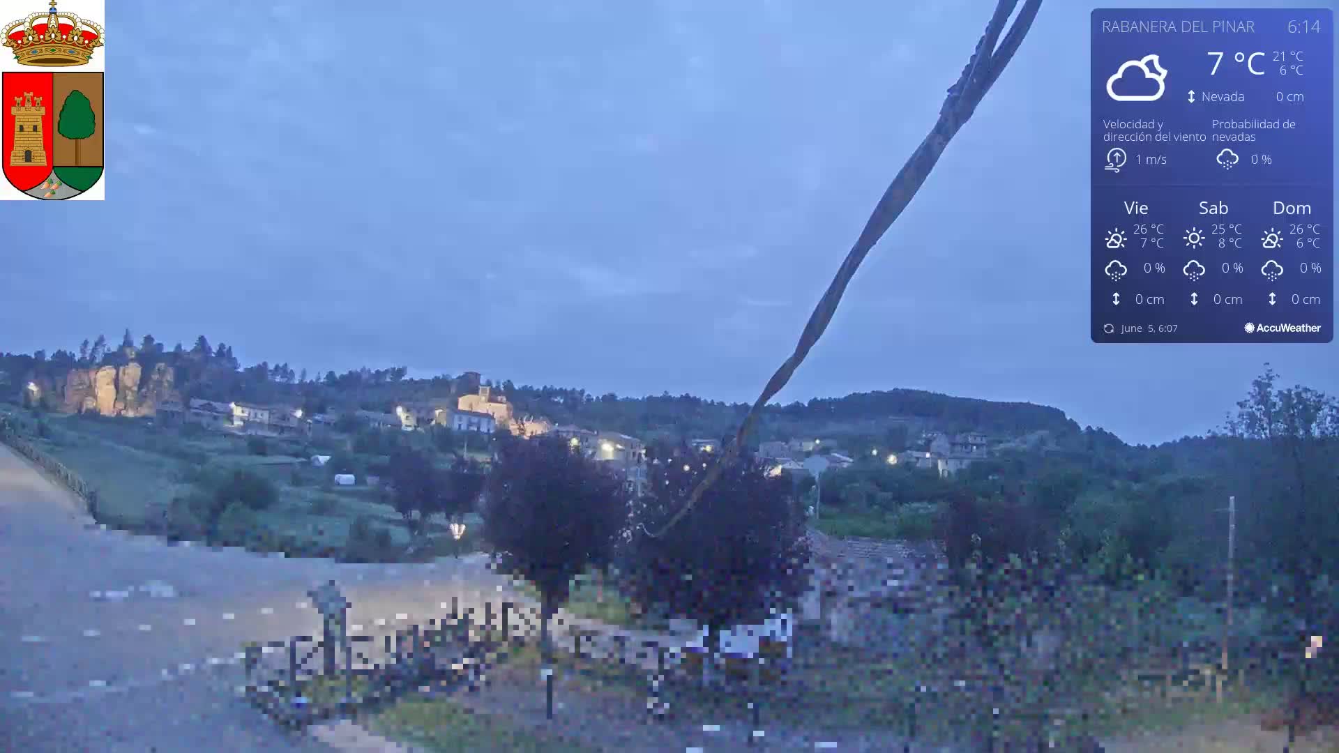 A small town nestled in a hilly landscape is visible under a twilight sky.