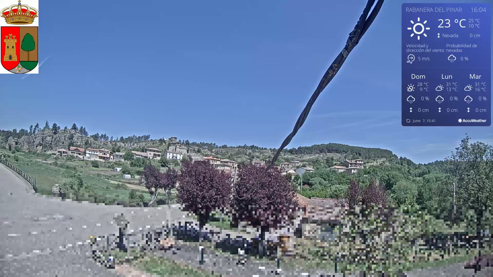 A sunny, clear day reveals a small village nestled among green hills and rocky outcrops.