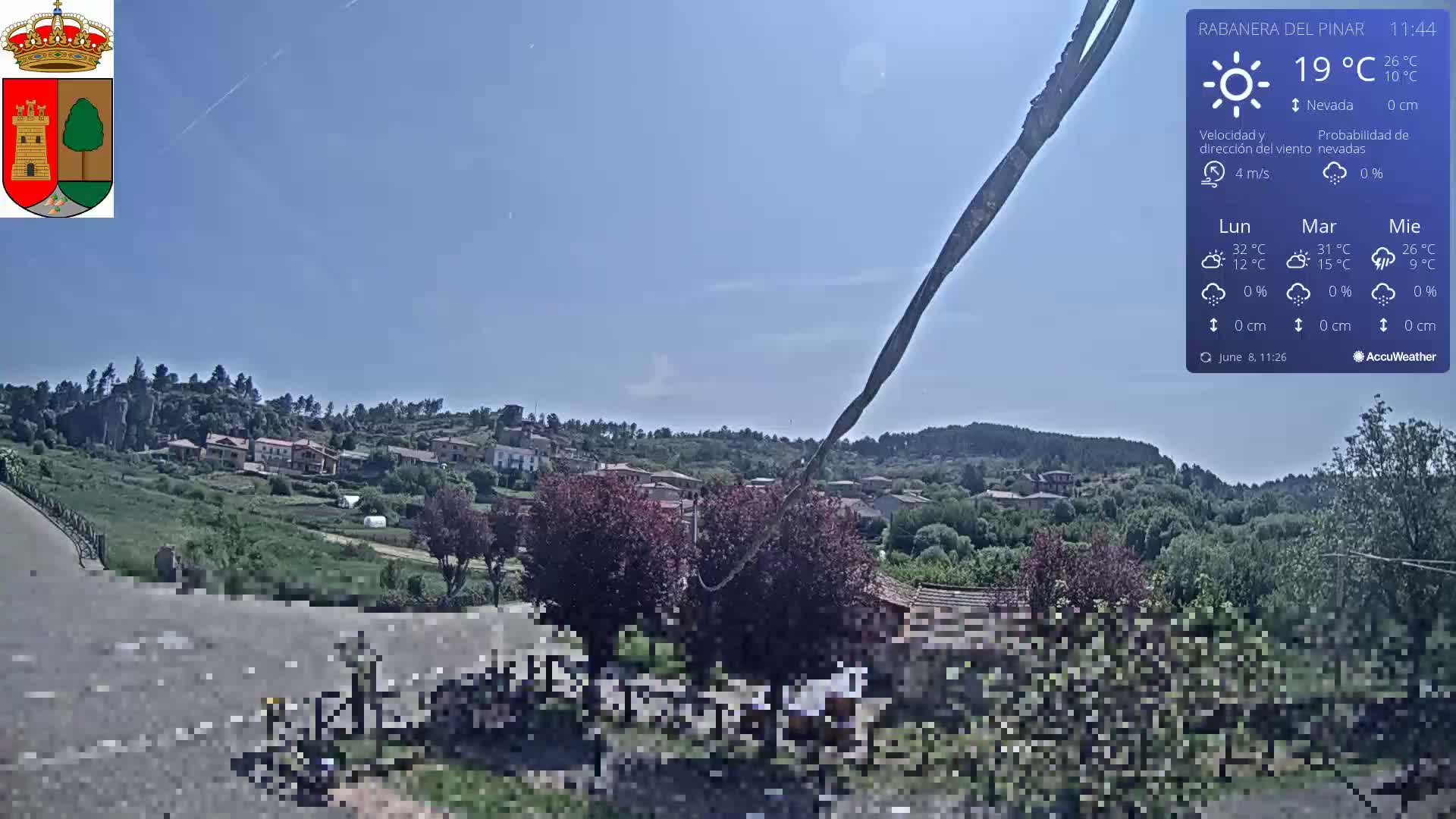 A sunny view of a small village nestled in a verdant hillside, with a clear blue sky.