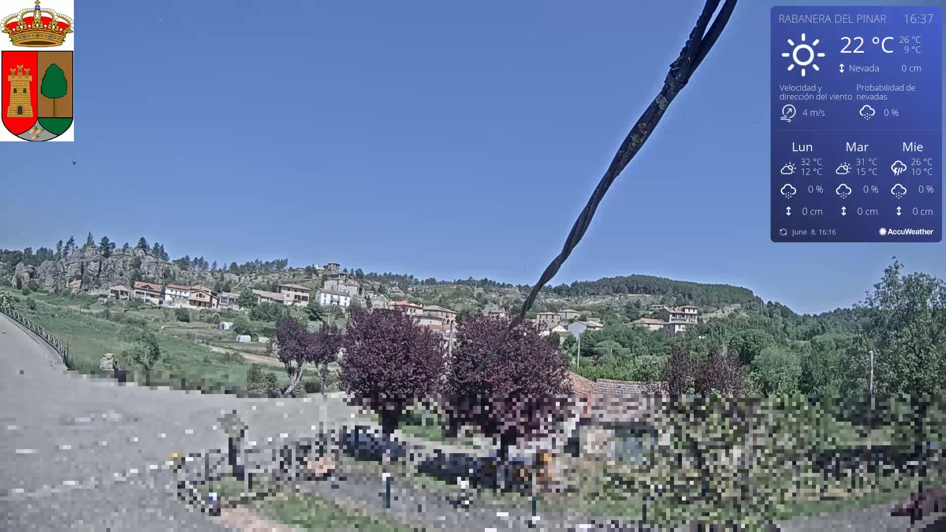 A sunny view of a small village nestled in a green valley, with rocky hills in the background.