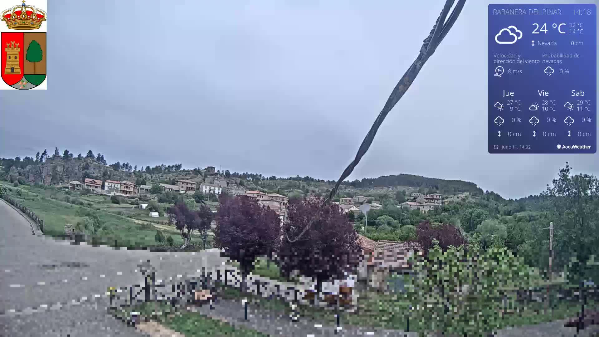 A small village nestled in a hilly landscape under an overcast sky is viewed from a roadside vantage point.