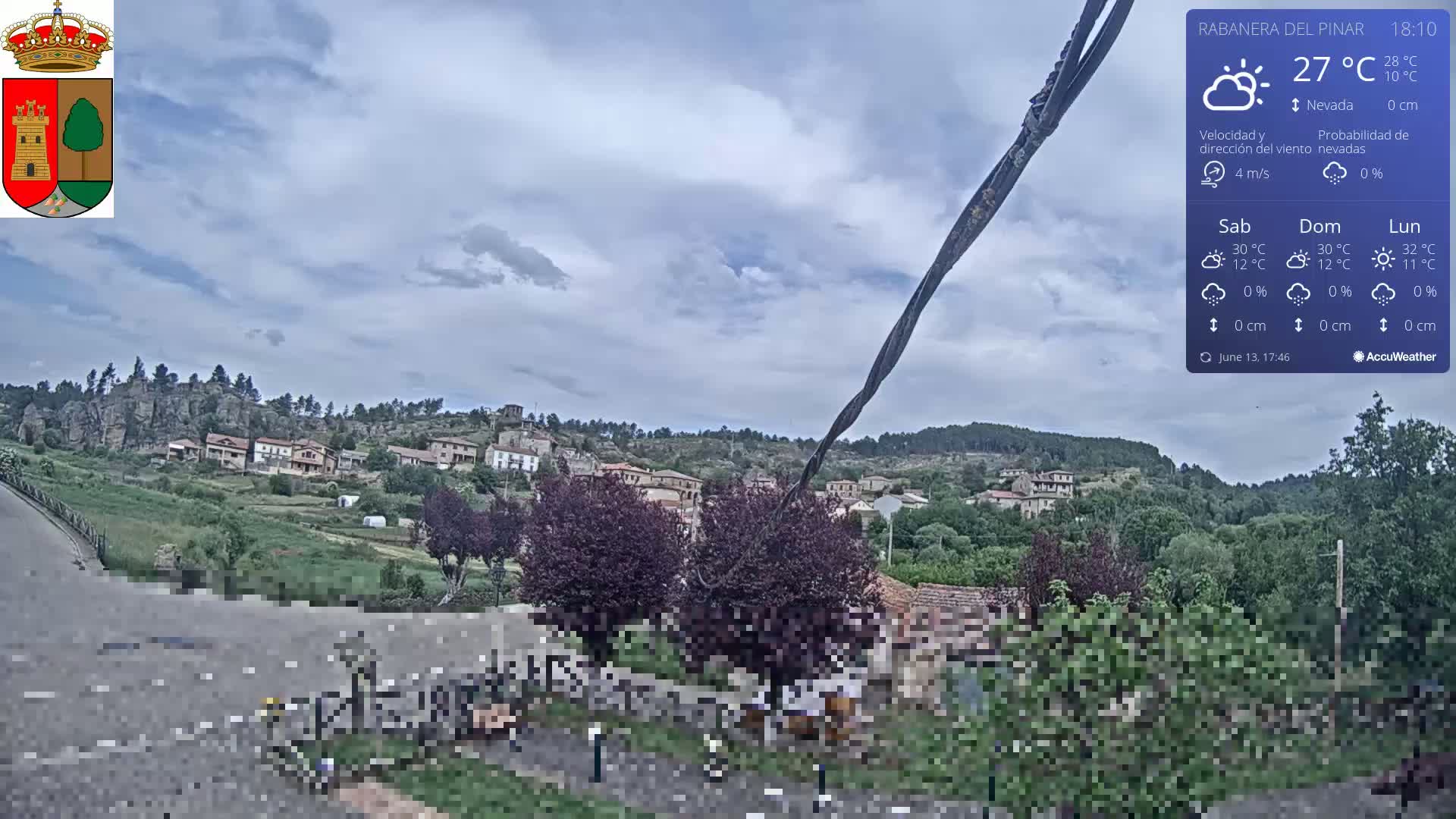 A partly cloudy day reveals a small village nestled in a green valley, with rocky hills rising behind it.