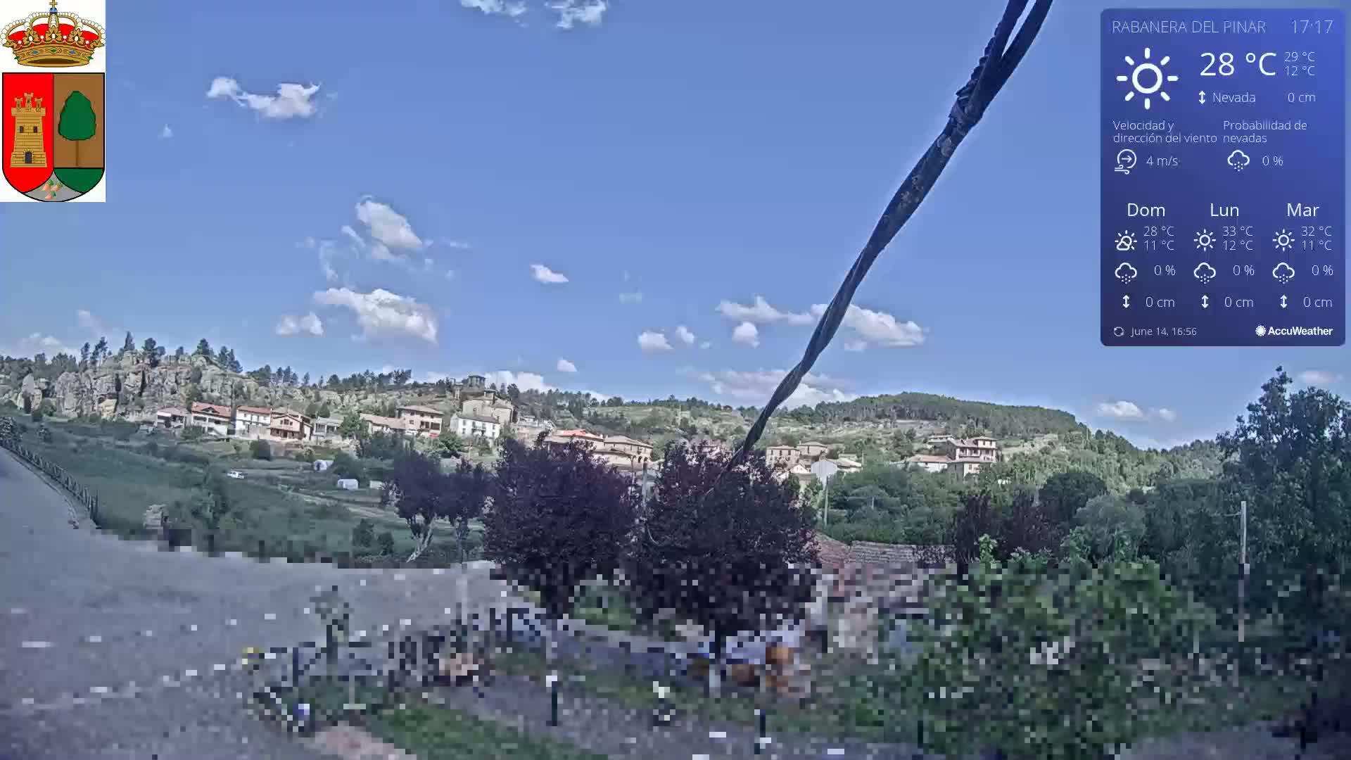 A partly cloudy sky overlooks a small village nestled in a hilly landscape.