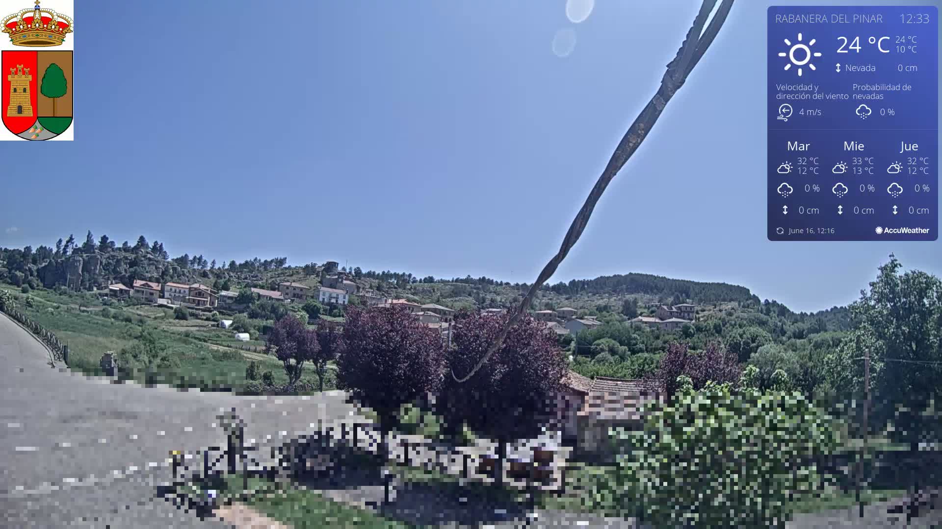 A sunny, clear day reveals a small village nestled in a green, hilly landscape.