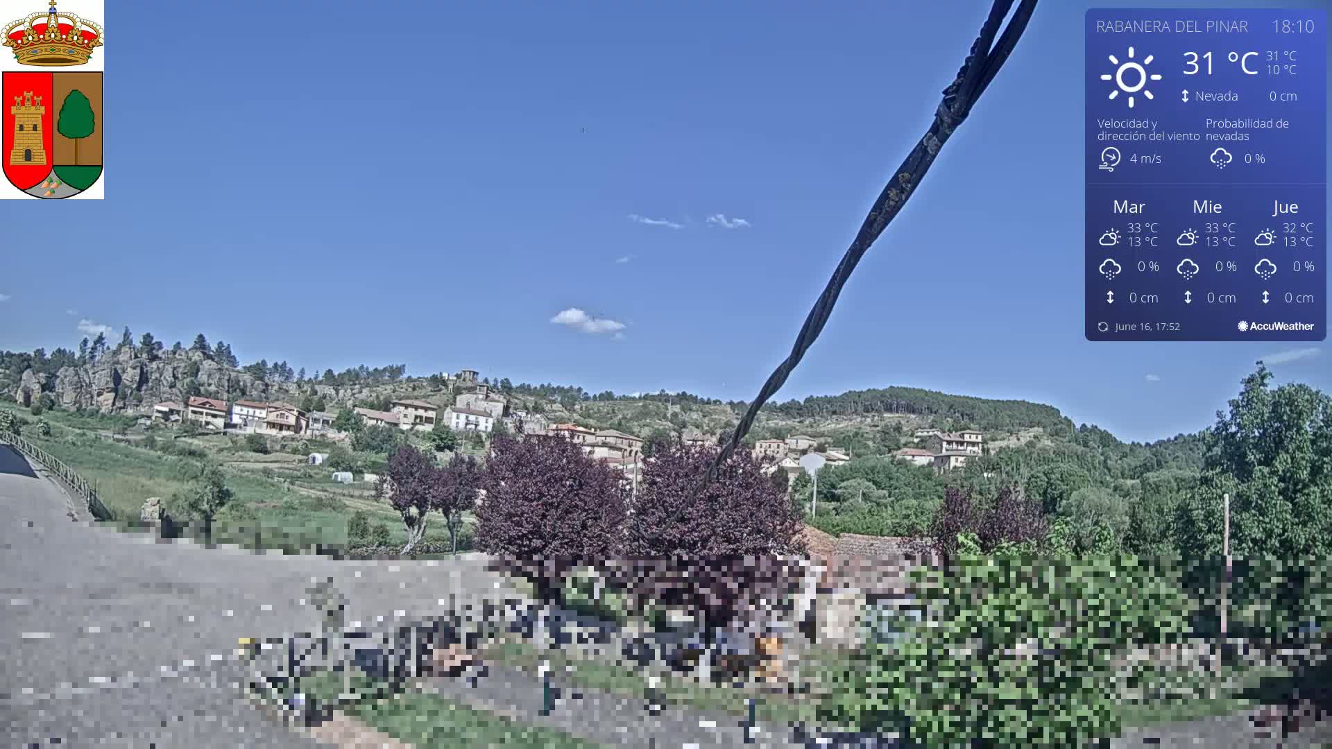 A sunny view of a small village nestled on a hillside, with dark green and purple trees in the foreground.