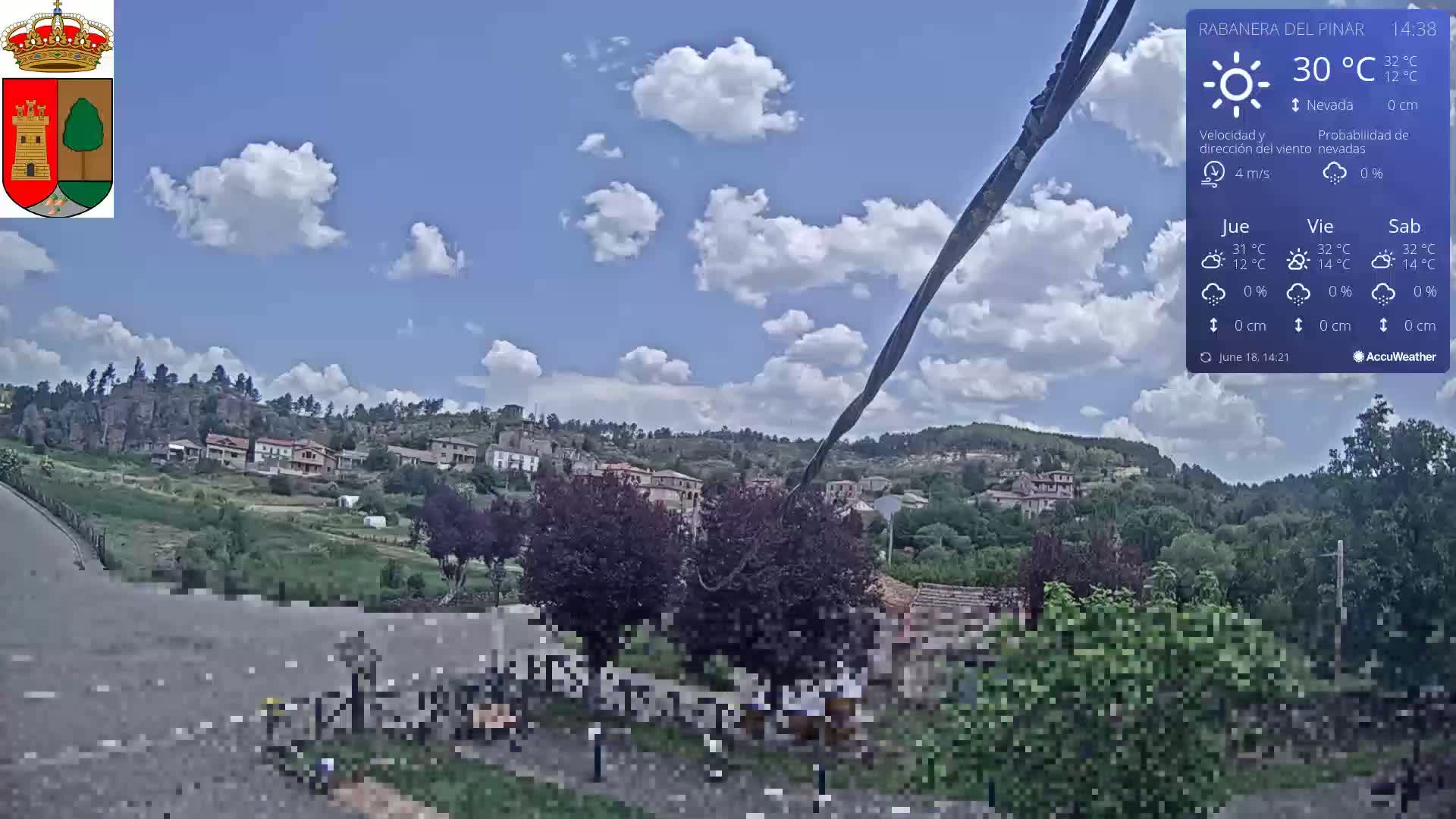 A partly cloudy day reveals a small village nestled among hills and trees, with a road leading to the foreground.