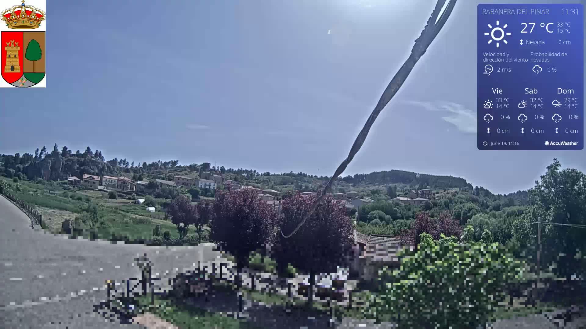 A sunny view of a small village nestled in a hilly landscape with green vegetation and a clear blue sky.