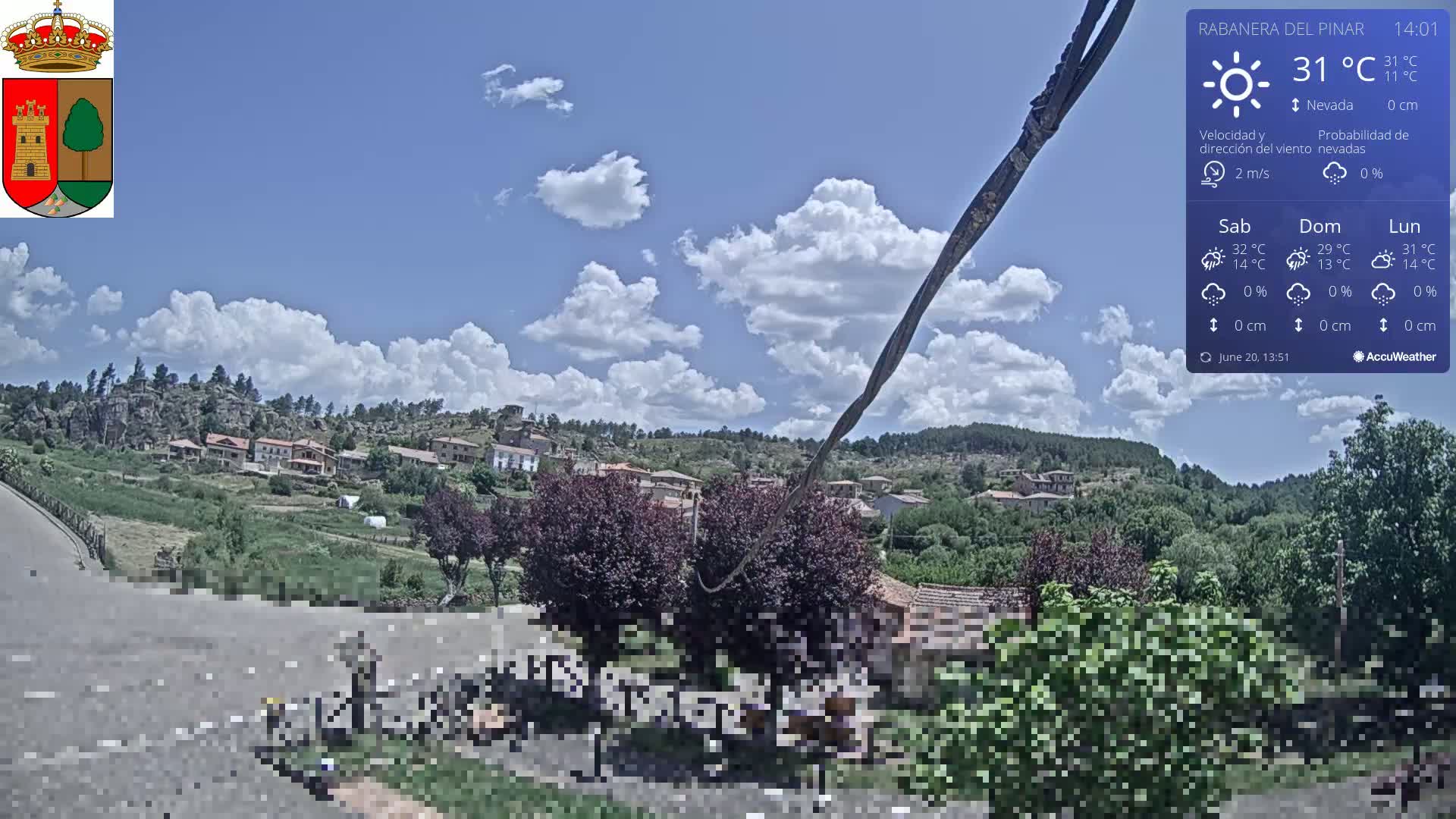 A partly cloudy day shows a village nestled in a hilly, green landscape.