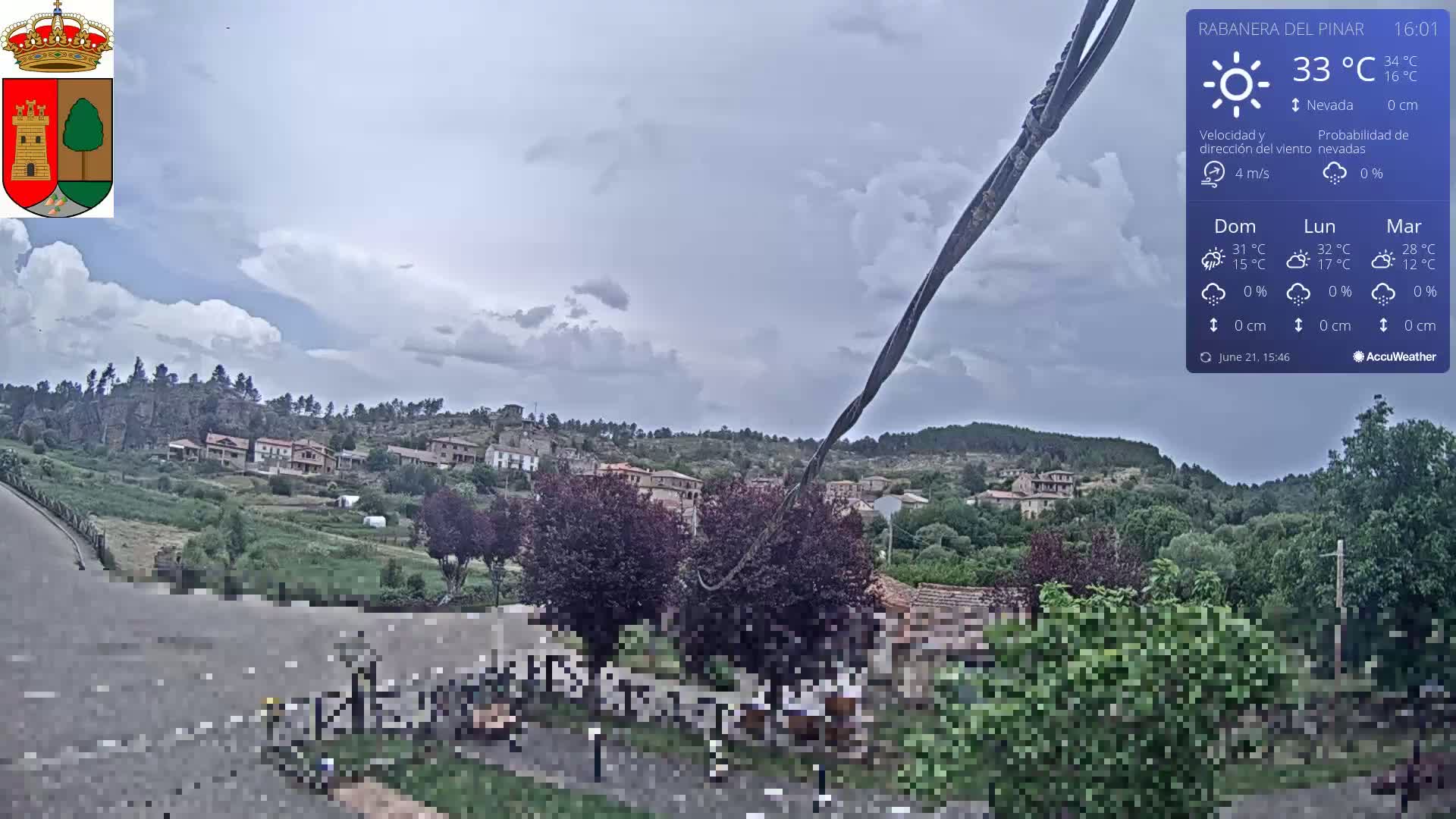 A partly cloudy sky hangs over a small village nestled in a verdant hillside.