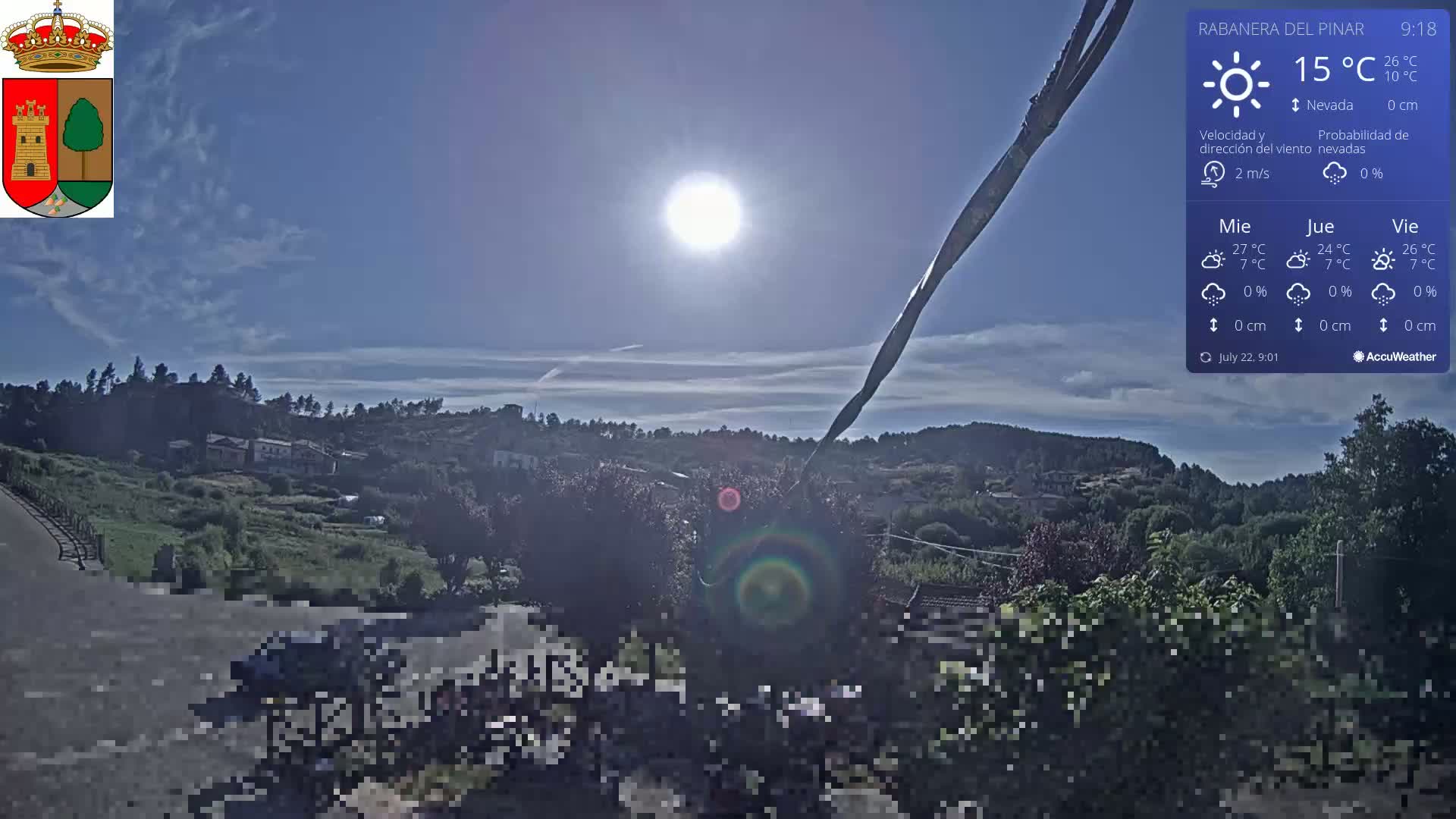 A sunny, mostly clear day overlooks a hilly landscape with a town nestled among green vegetation.