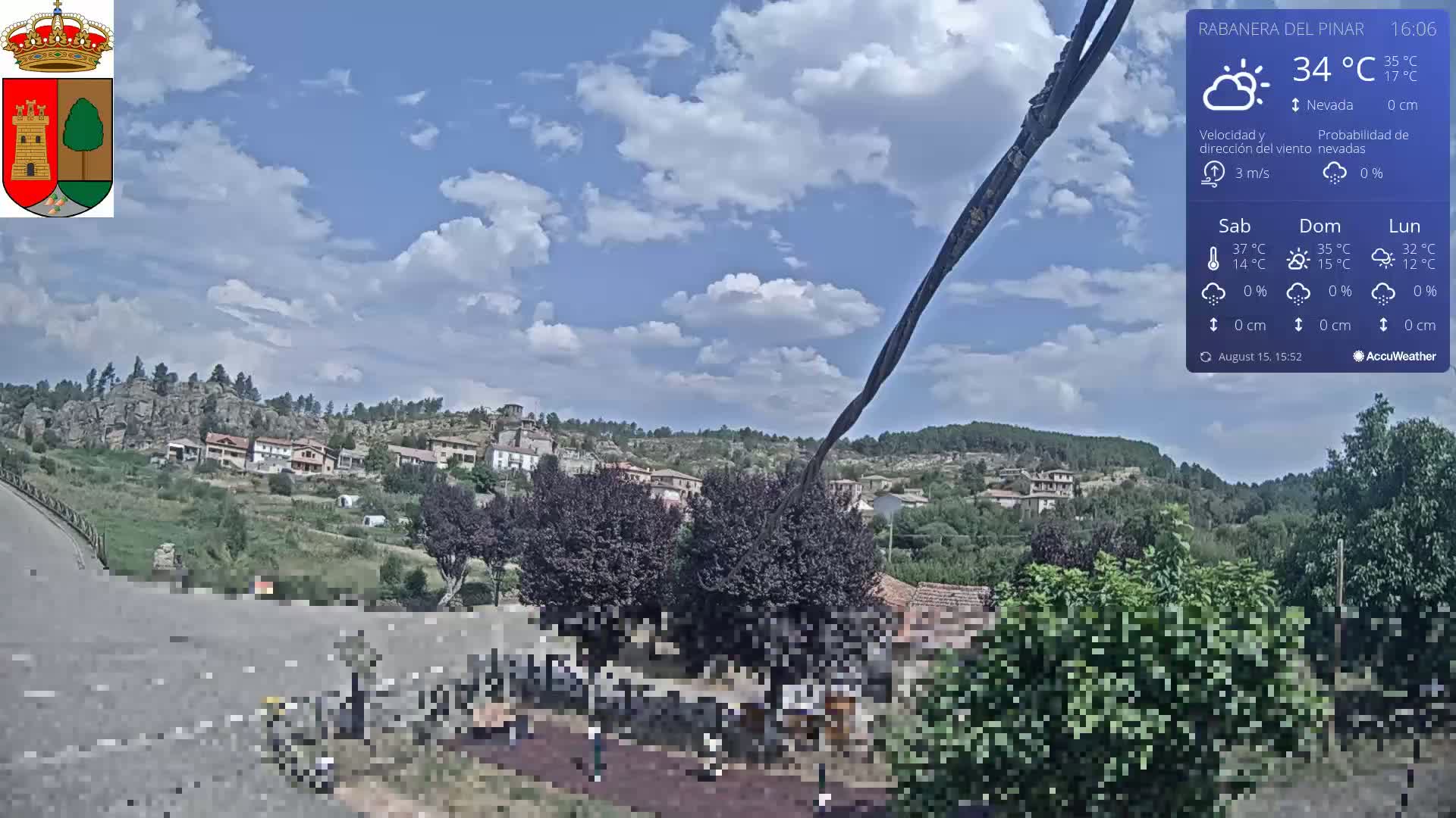A sunny, mostly clear day overlooks a hilly landscape with a town nestled among green vegetation.