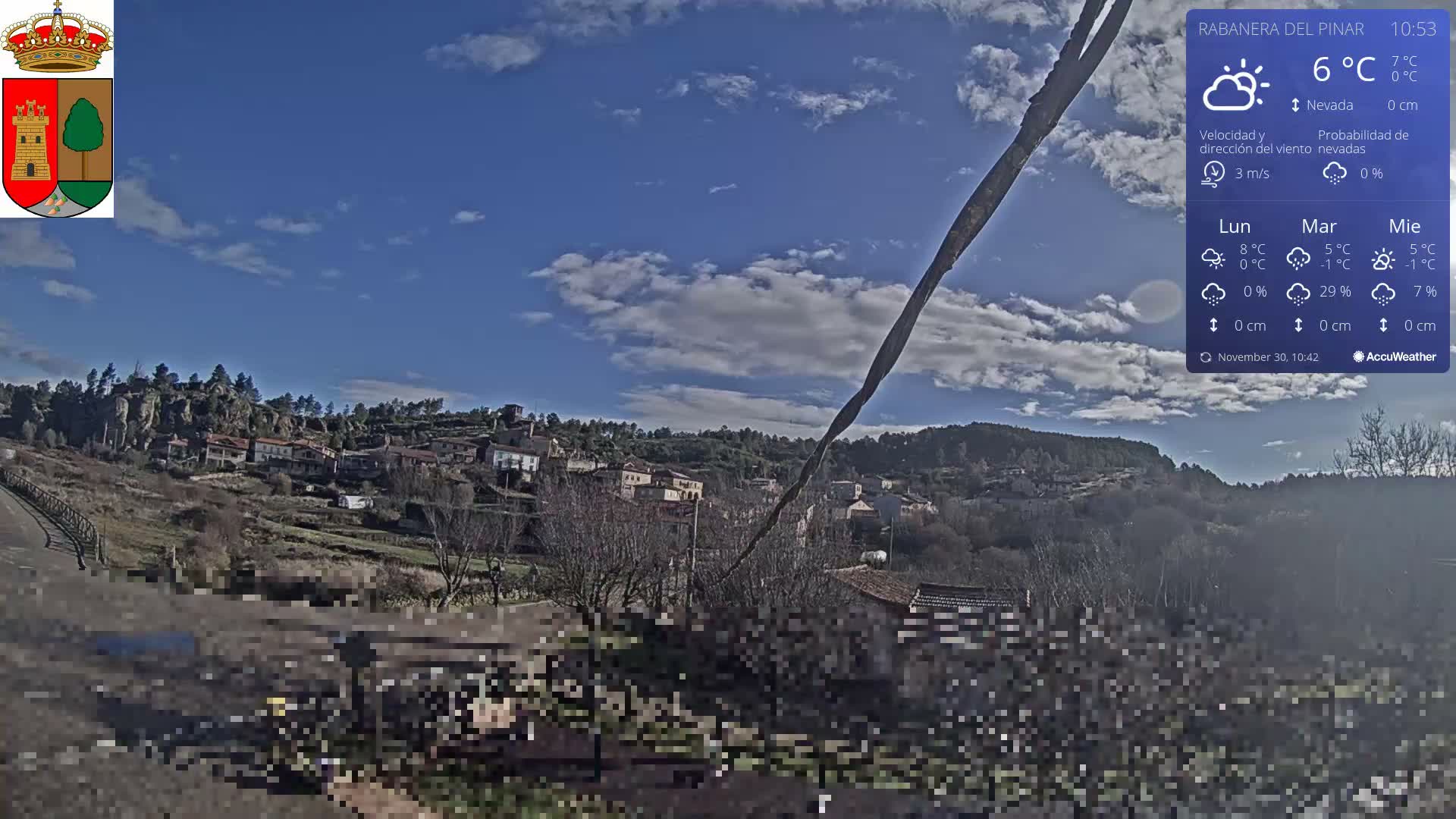 A partially cloudy sky overlooks a hillside village with scattered buildings and mostly barren trees, while a heavily pixelated foreground obscures a curving road.