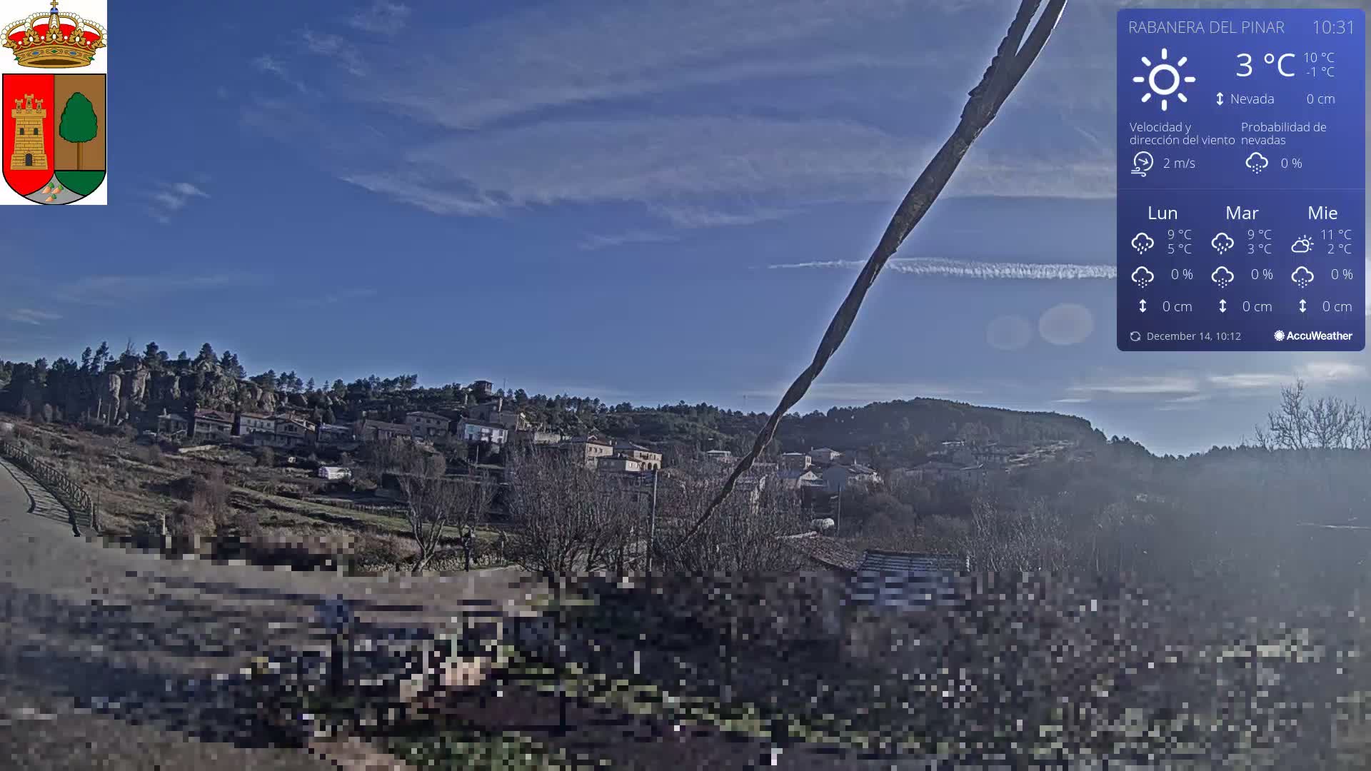 A partially cloudy sky overlooks a hillside village with scattered buildings and mostly barren trees, while a heavily pixelated foreground obscures a curving road.