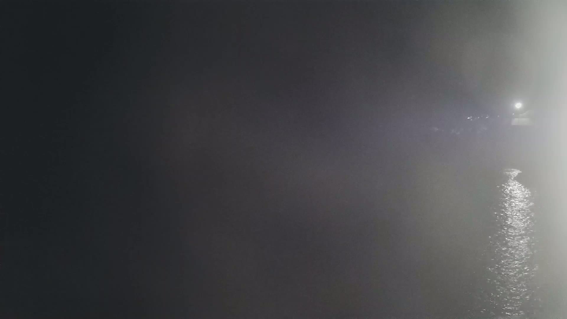 A nighttime view of a foggy body of water reflecting a light source in the distance.