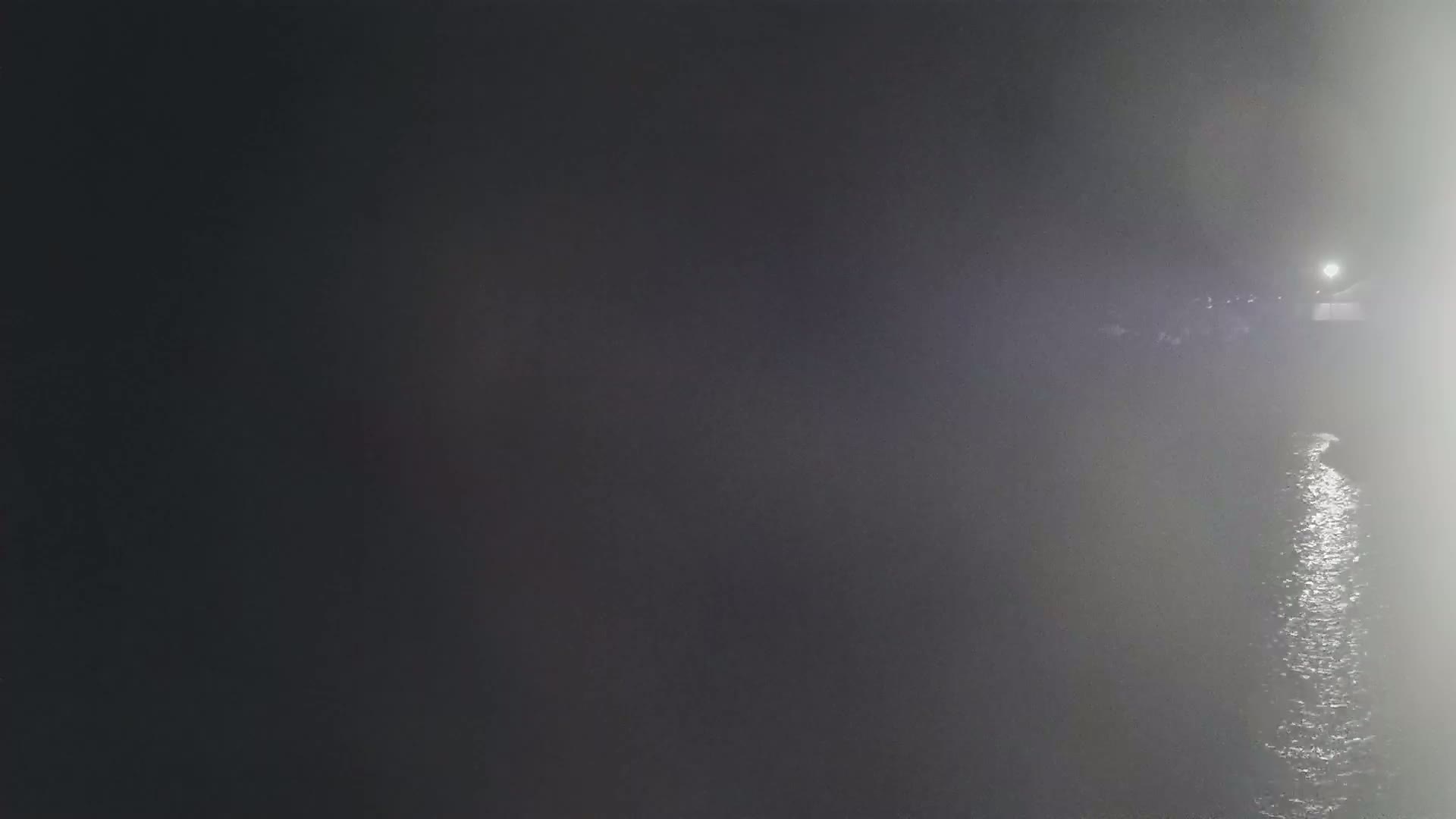 A dimly lit body of water at night is partially obscured by fog.