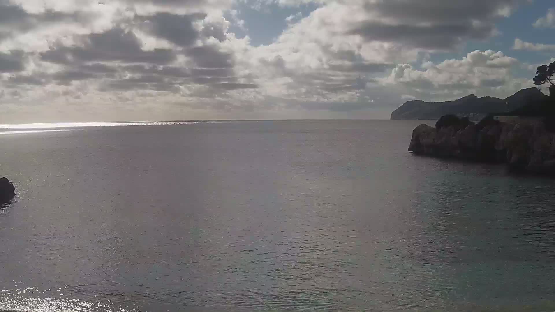 A calm sea under a partly cloudy sky stretches to a distant, hilly coastline.