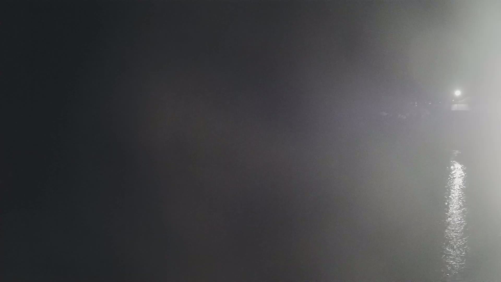 A dimly lit body of water is shrouded in fog at night, with a light source visible in the distance.